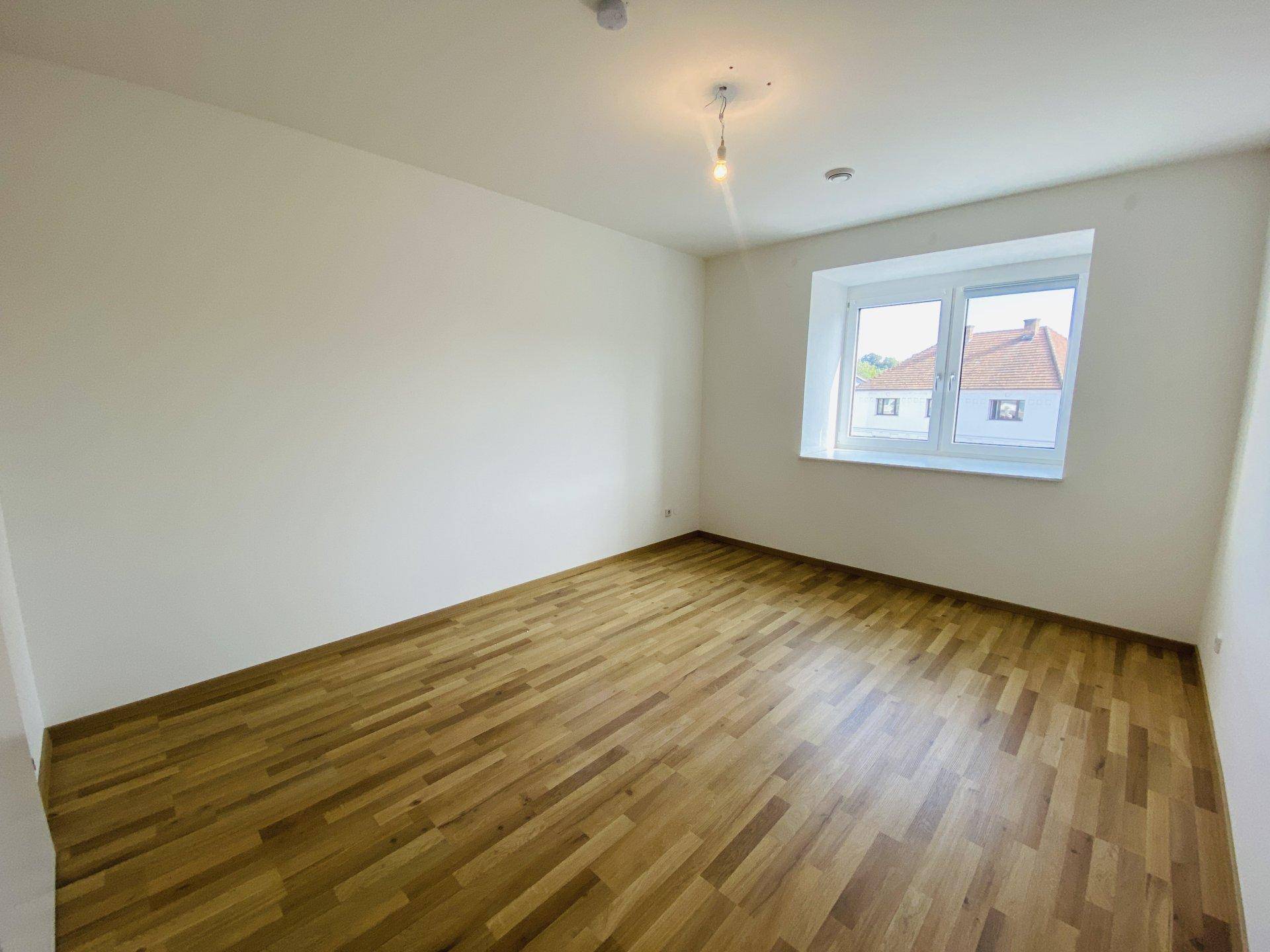 Geräumiges Schlafzimmer mit Holzparkettboden und einem Fenster mit Blick auf die Umgebung.