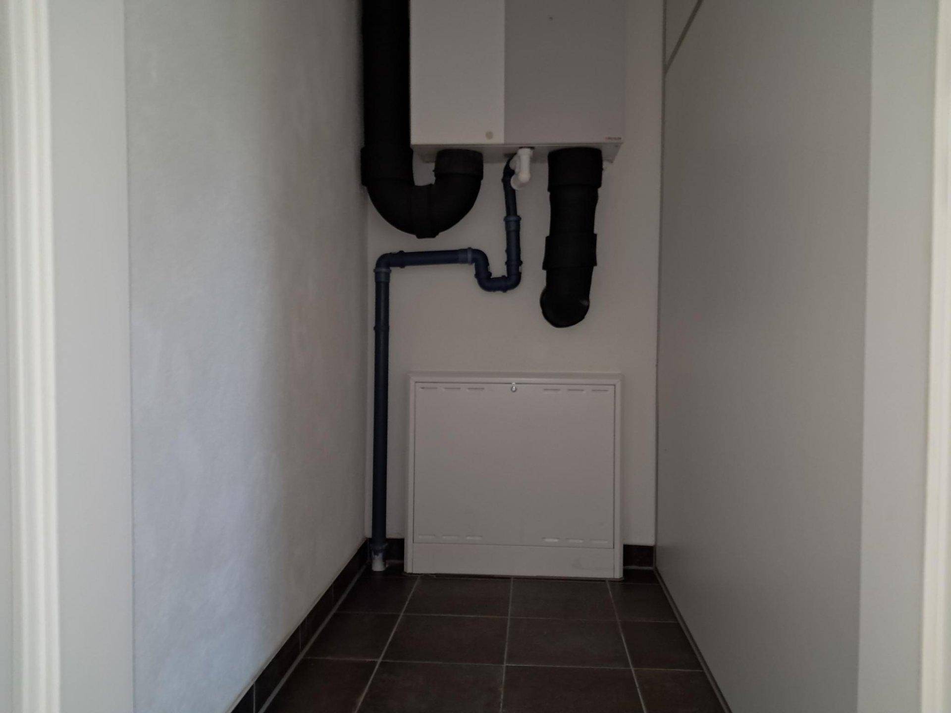 Praktischer Hauswirtschaftsraum mit sichtbaren Installationen und Fliesenboden.