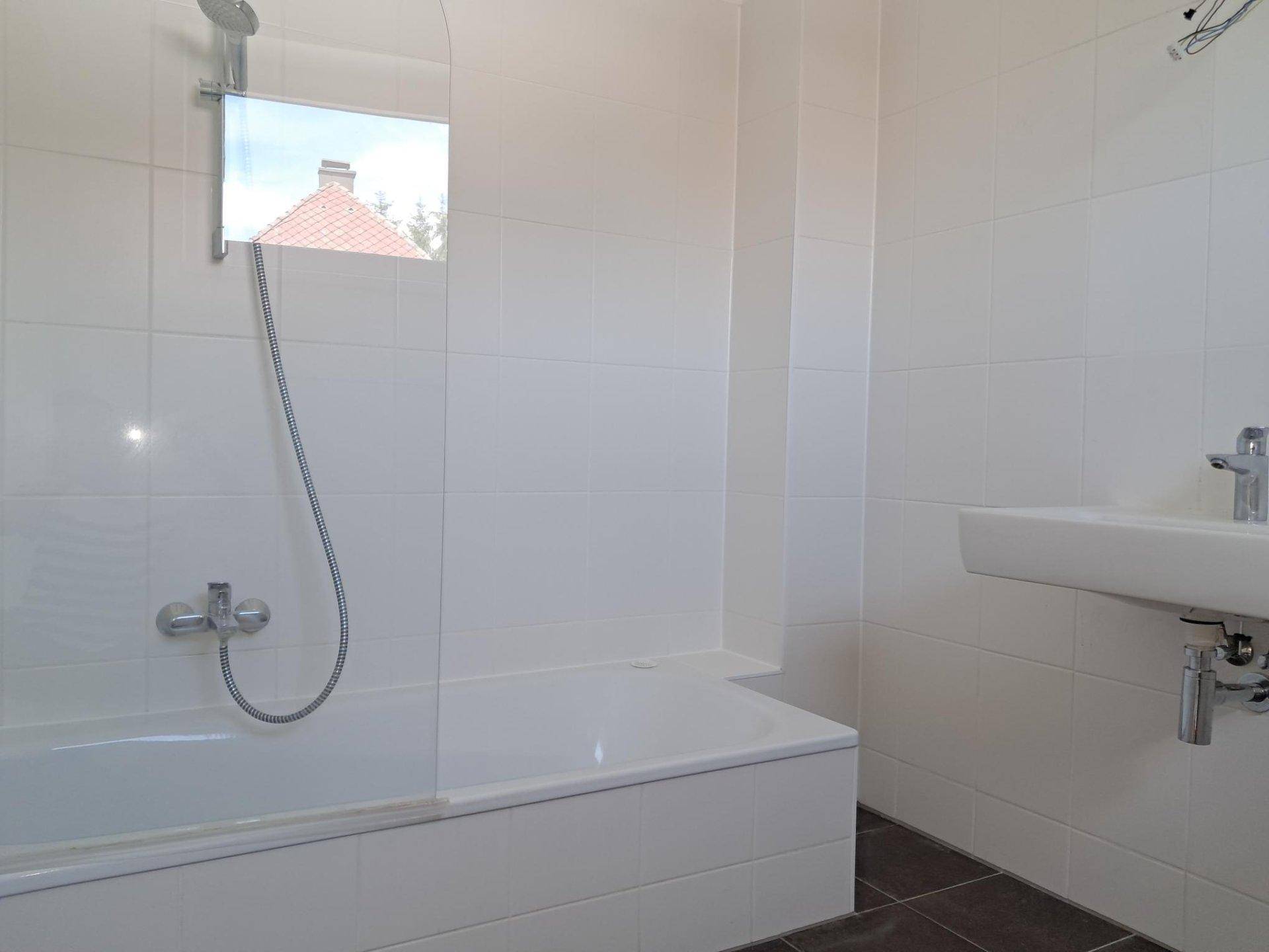 Modern gefliestes Badezimmer mit Badewanne, Duscharmatur und einem kleinen Fenster.