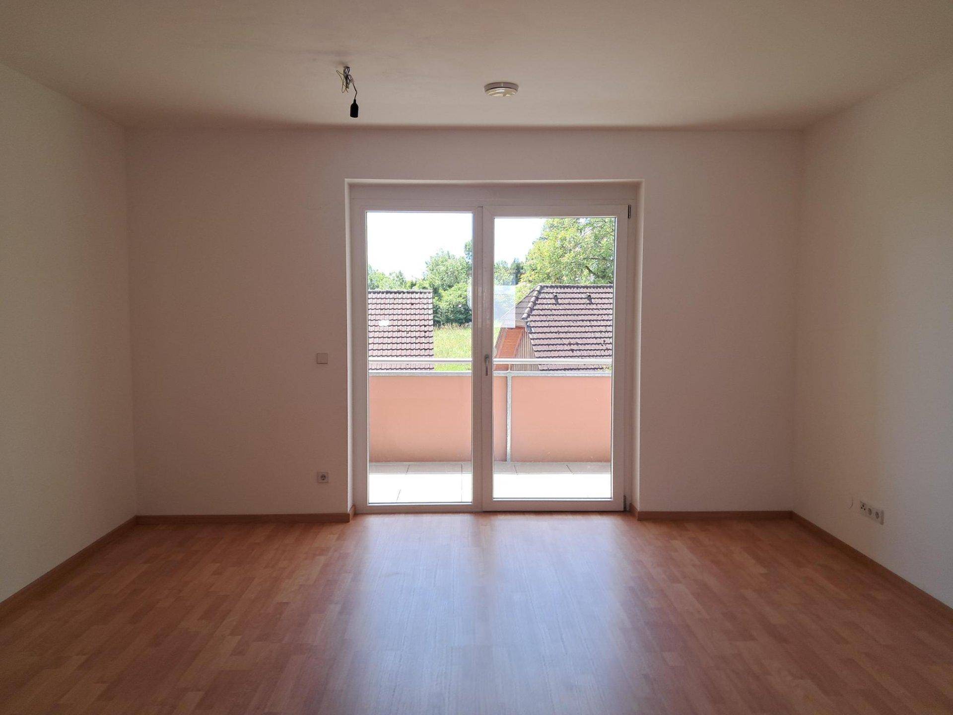 Geräumiger, heller Wohnraum mit Laminatboden und direktem Zugang zum Balkon.