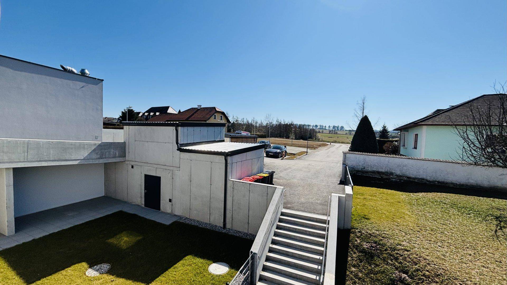 Rückseite des Neubaus mit kleinem Garten, Außentreppe und Blick auf die umliegende Landschaft.