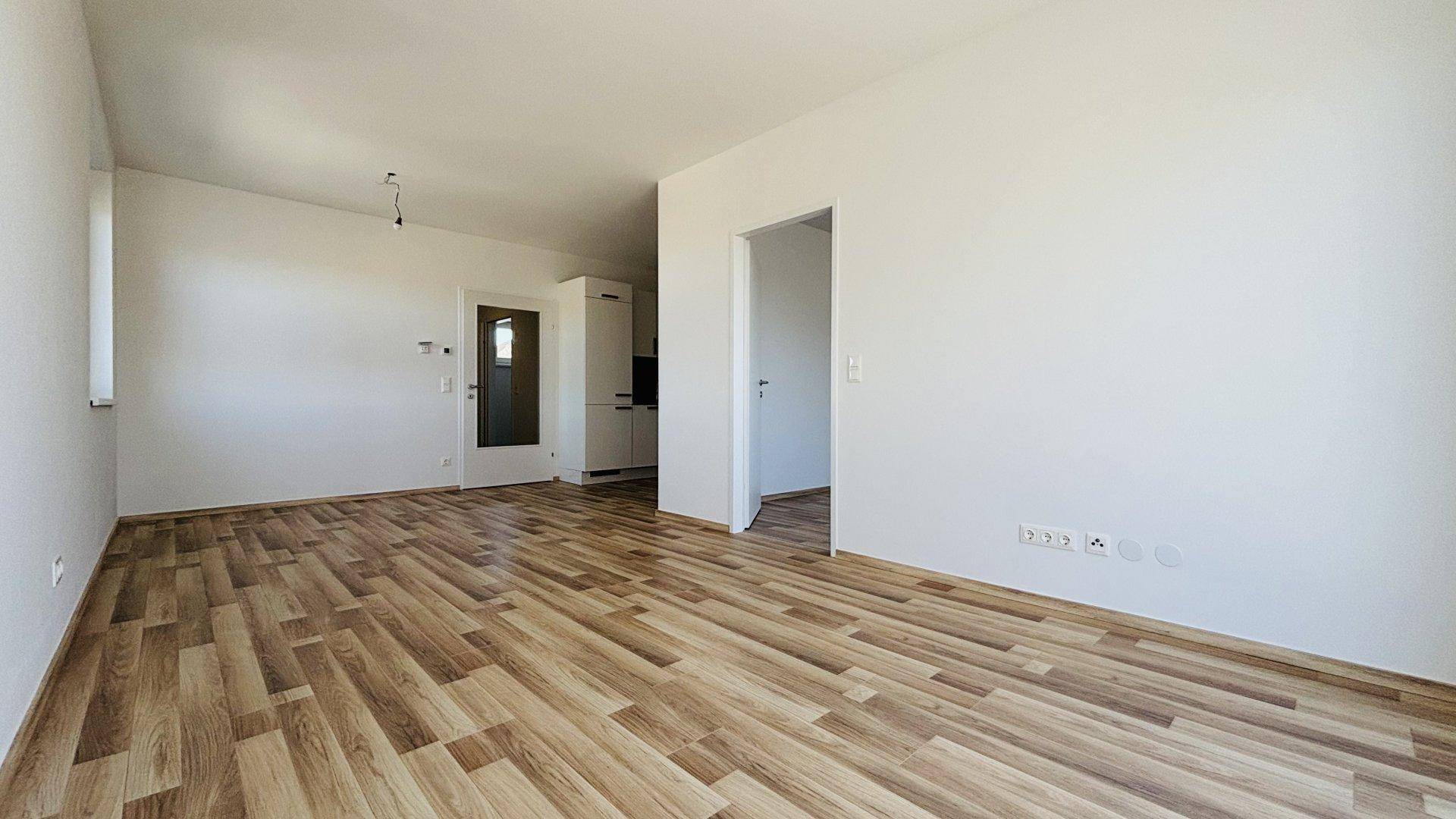 Heller Wohnbereich mit Laminatboden und offenem Durchgang zu weiteren Räumen.