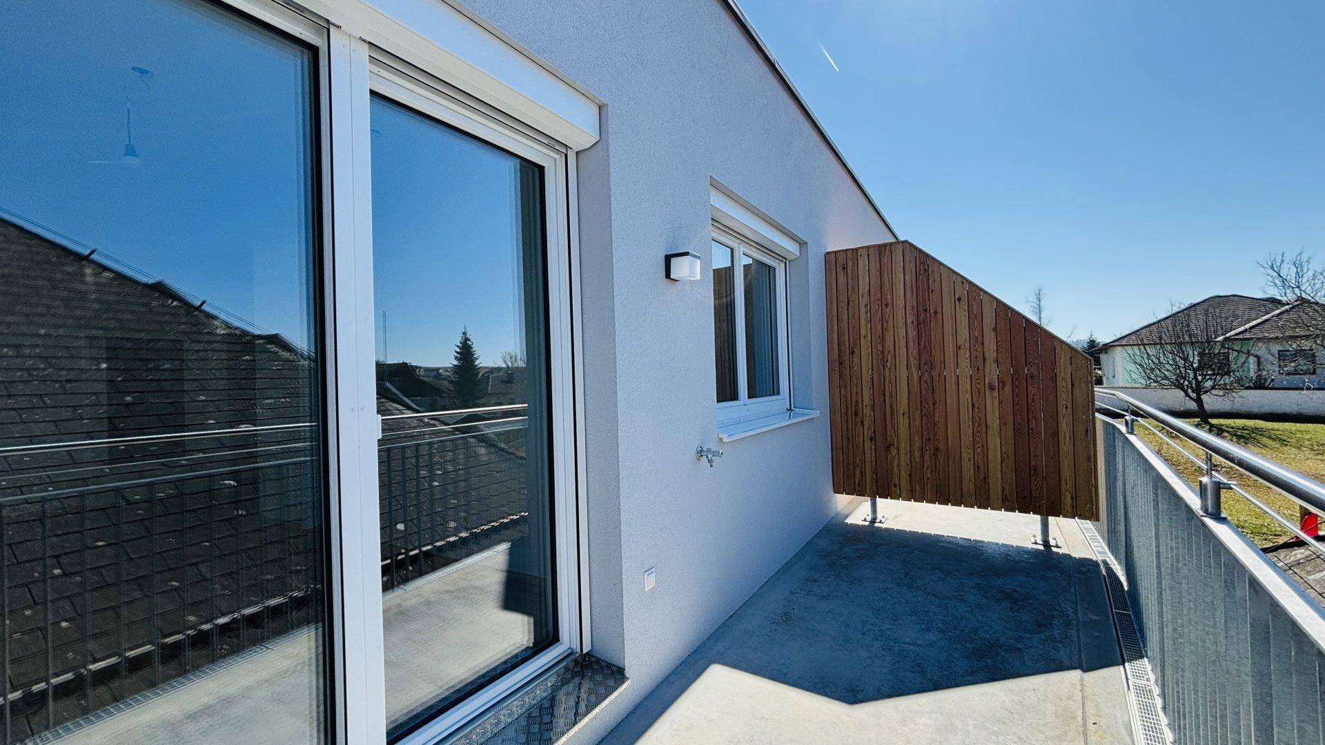 Moderner Balkon mit Holzsichtschutz, Metallgeländer und Schiebetür zum Innenbereich.