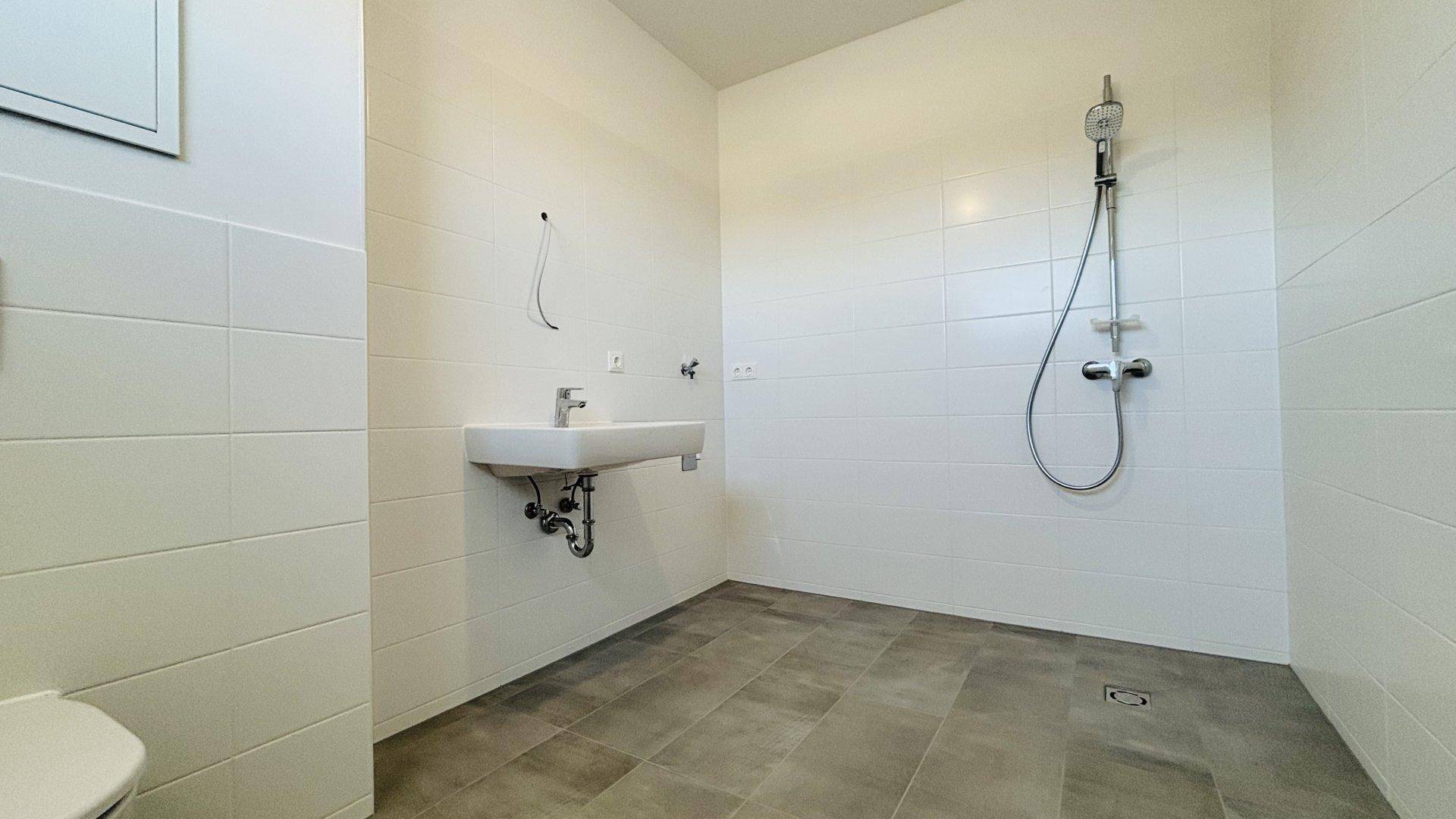 Modernes Badezimmer mit weißen Fliesen, ebenerdiger Dusche und einem Waschbecken.