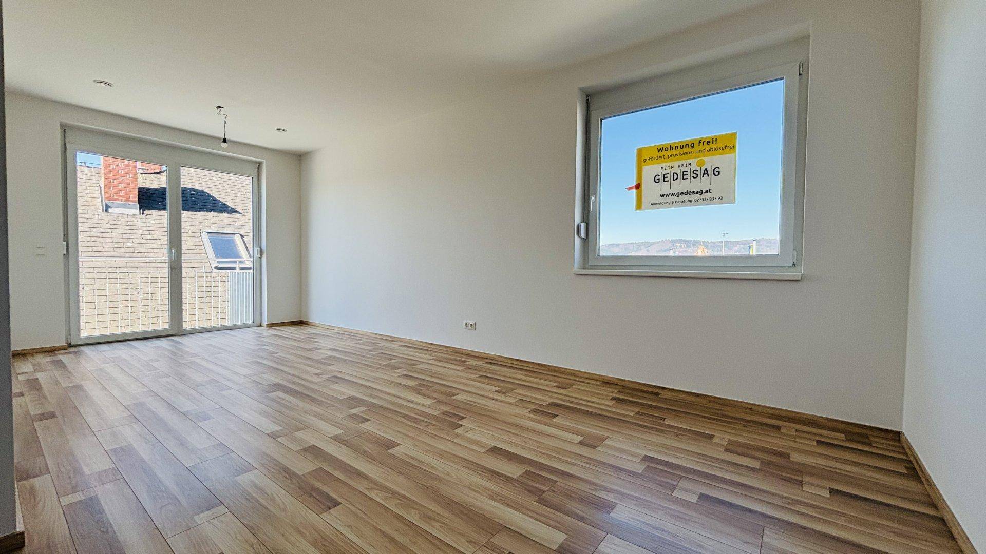 Geräumiger, heller Raum mit Laminatboden, großem Fenster und Zugang zu einem Balkon.