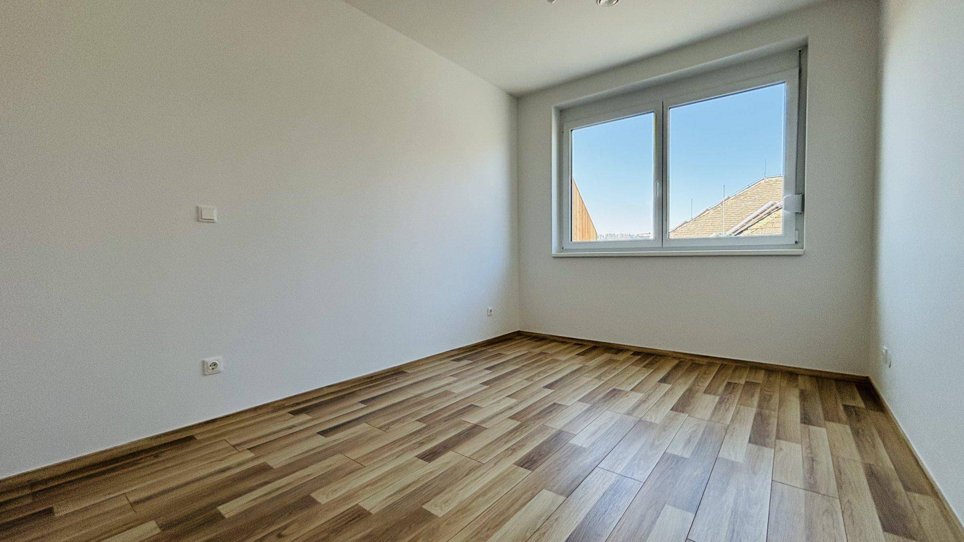 Helles Schlafzimmer mit Laminatboden und einem großen Fenster für viel Tageslicht.