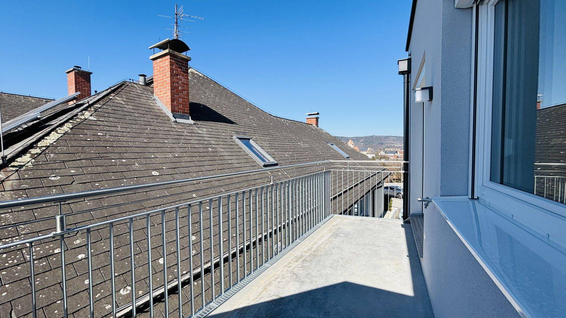 Geräumiger Balkon mit Metallgeländer und Blick über die Dächer der Nachbarschaft.