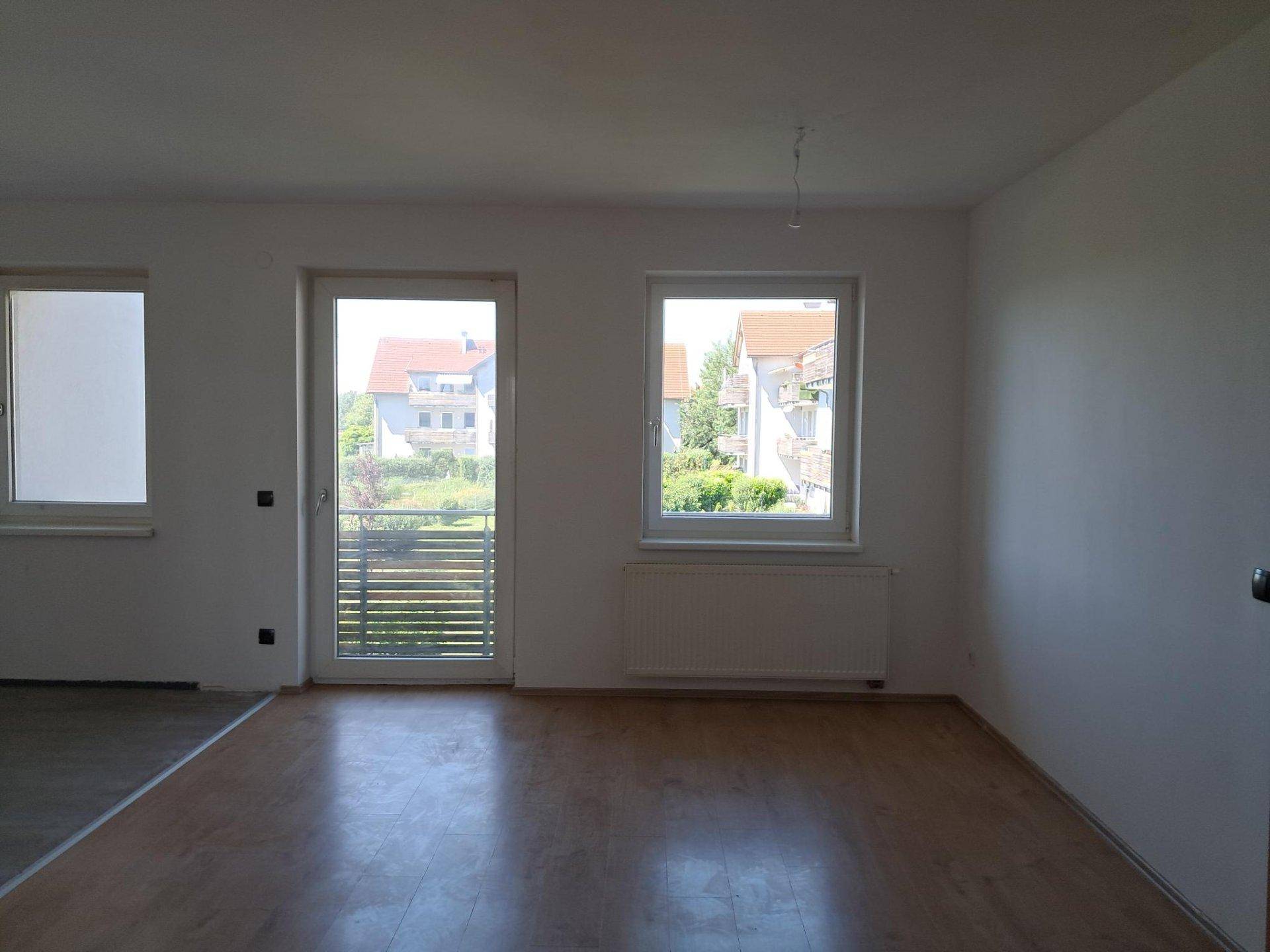 Heller Wohnraum mit Holzboden, weiß gestrichenen Wänden und Zugang zu einem Balkon.