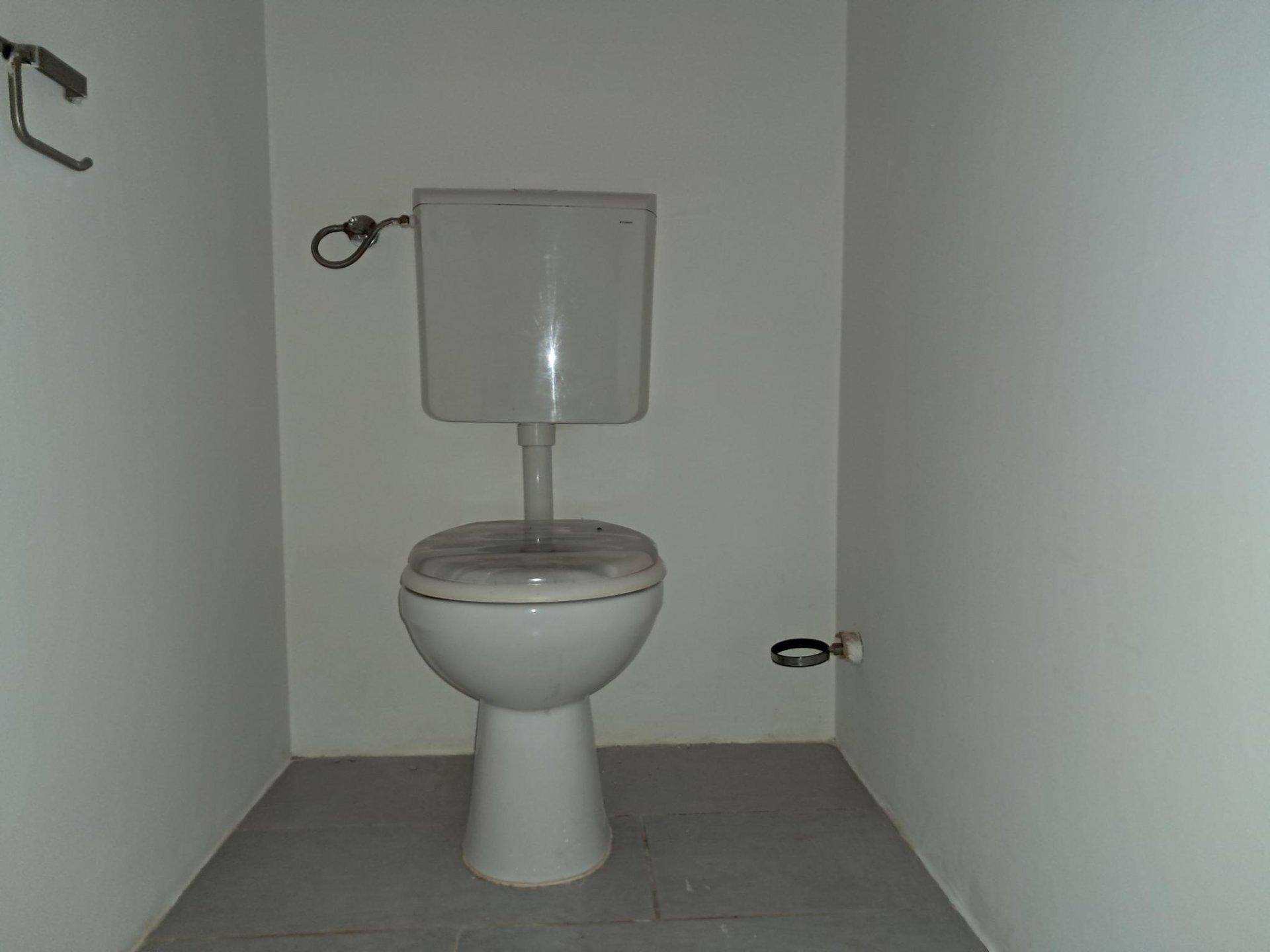 Separates WC mit einfacher Toilette und weißen Wänden, funktional und sauber.