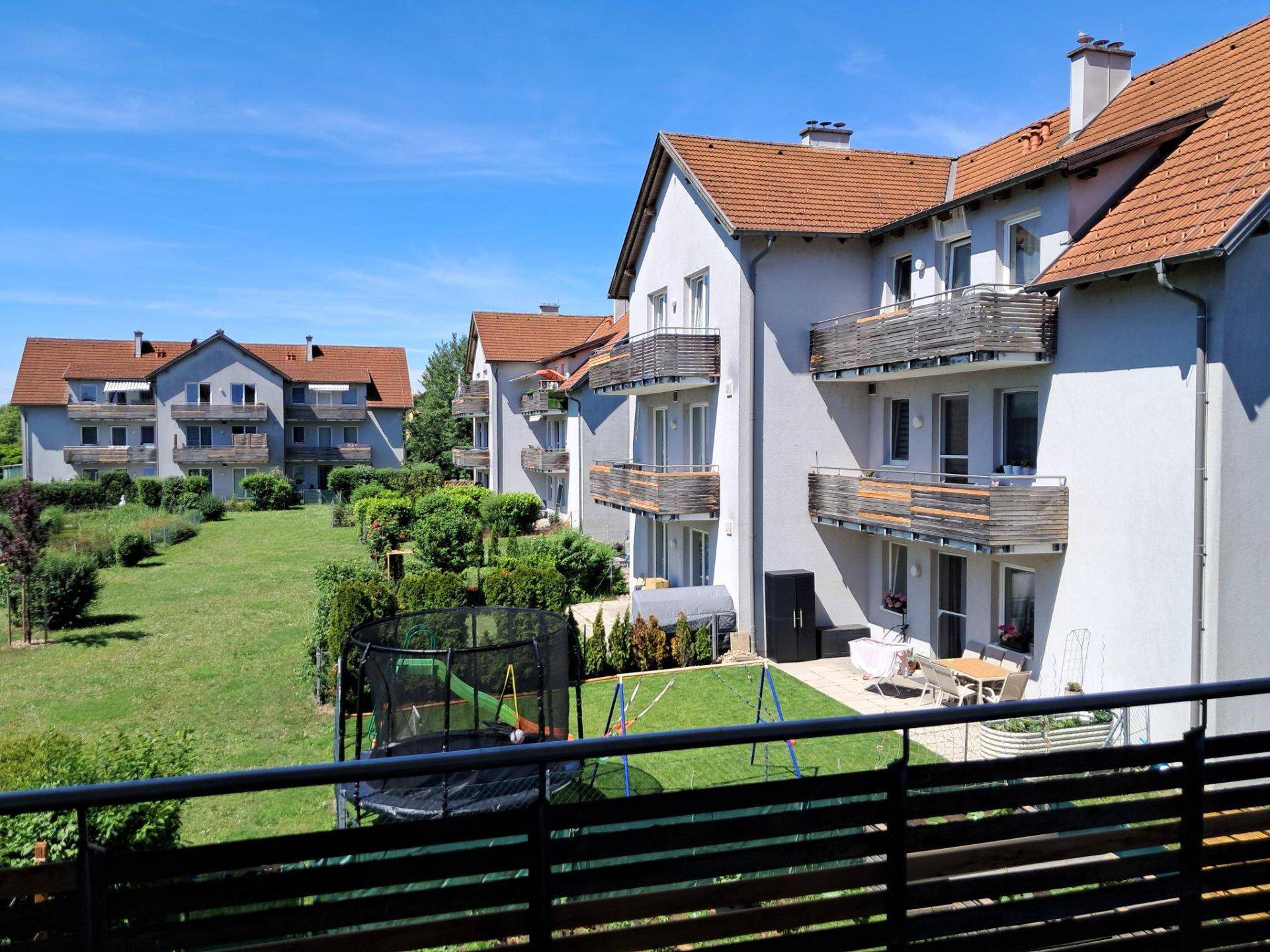 Blick vom Balkon auf die Wohnanlage mit großem Rasenbereich und Kinderspielgeräten.