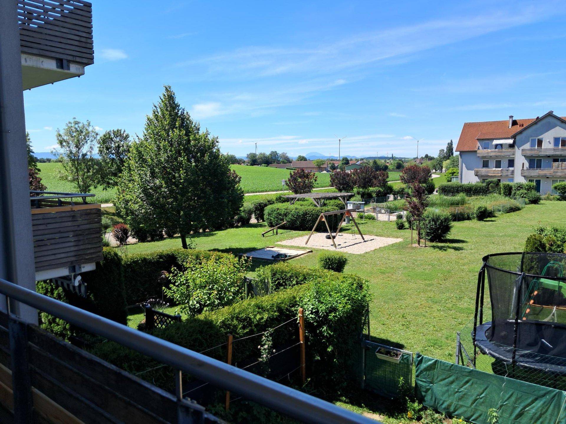 Weitläufiger Blick vom Balkon über die grüne Wohnanlage mit Spielplatz und Landschaft.