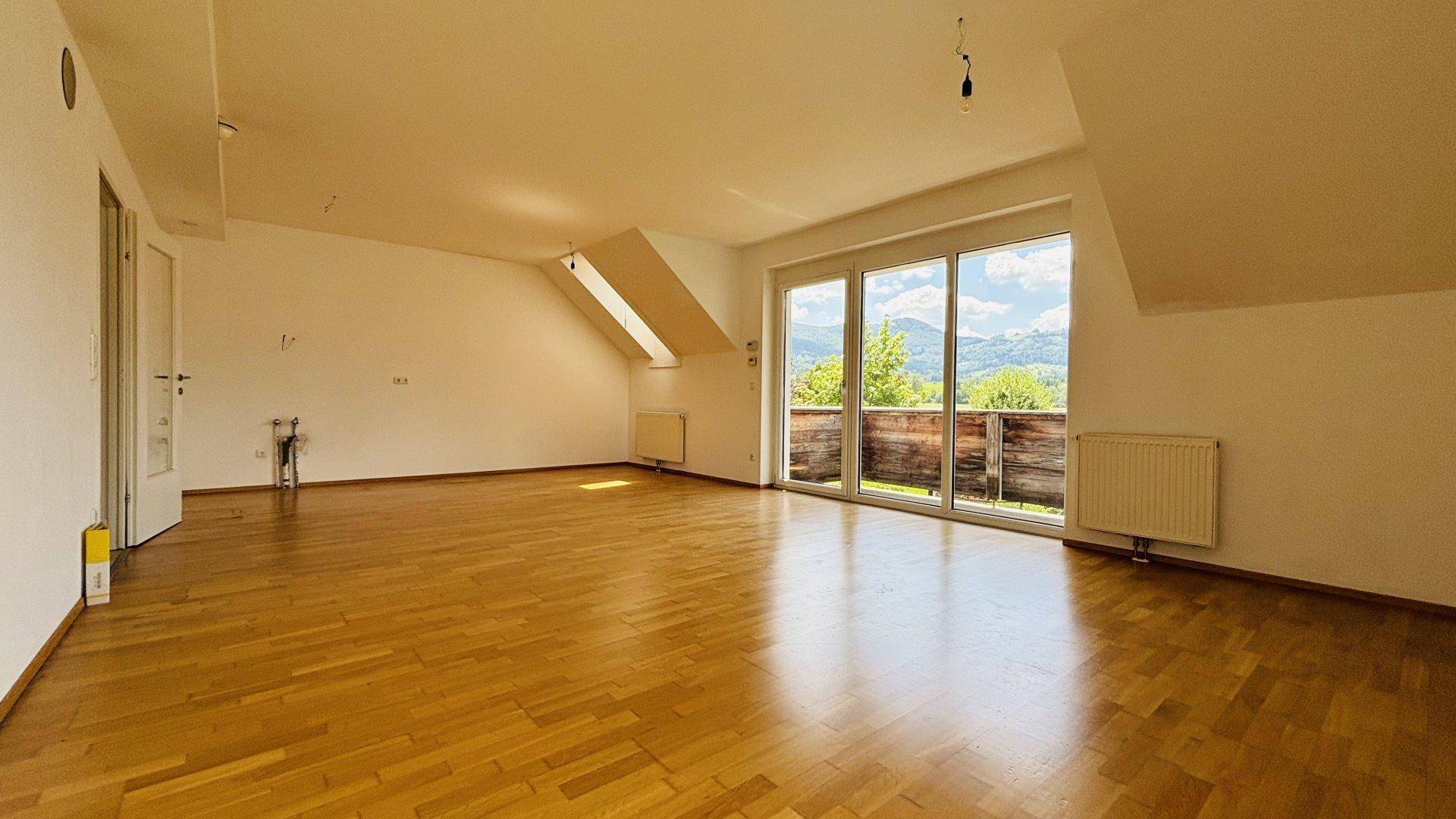 Lichtdurchflutetes Wohnzimmer mit Parkettboden, Dachfenster und Schiebetür zum Balkon mit Bergblick.