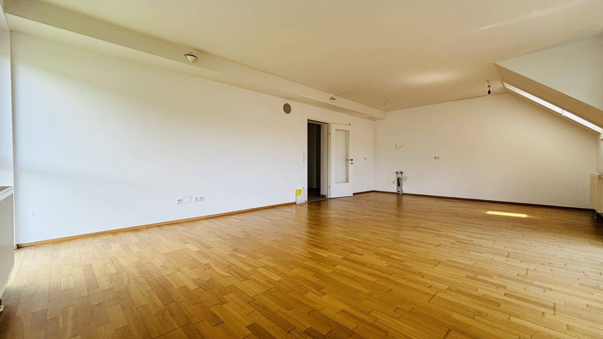 Heller Wohnbereich mit Holzboden und weiß gestrichenen Wänden, bereit zur individuellen Gestaltung.