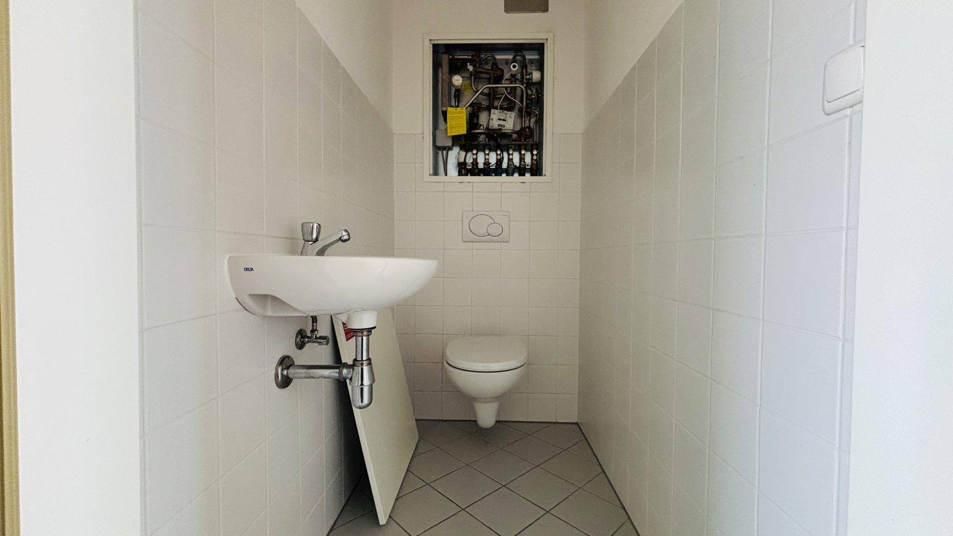 Kleines Gäste-WC mit Waschbecken und Toilette, komplett gefliest in neutralen Farben.