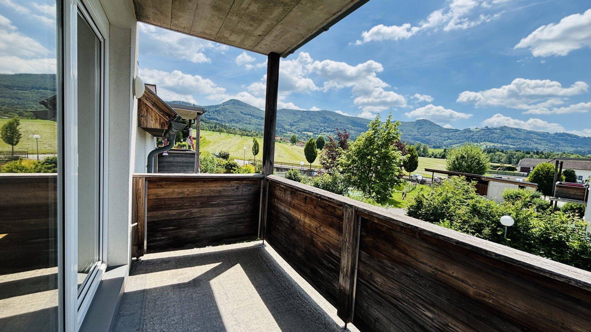 Überdachter Balkon mit Holzelementen und weitem Blick auf die umliegende grüne Hügellandschaft.