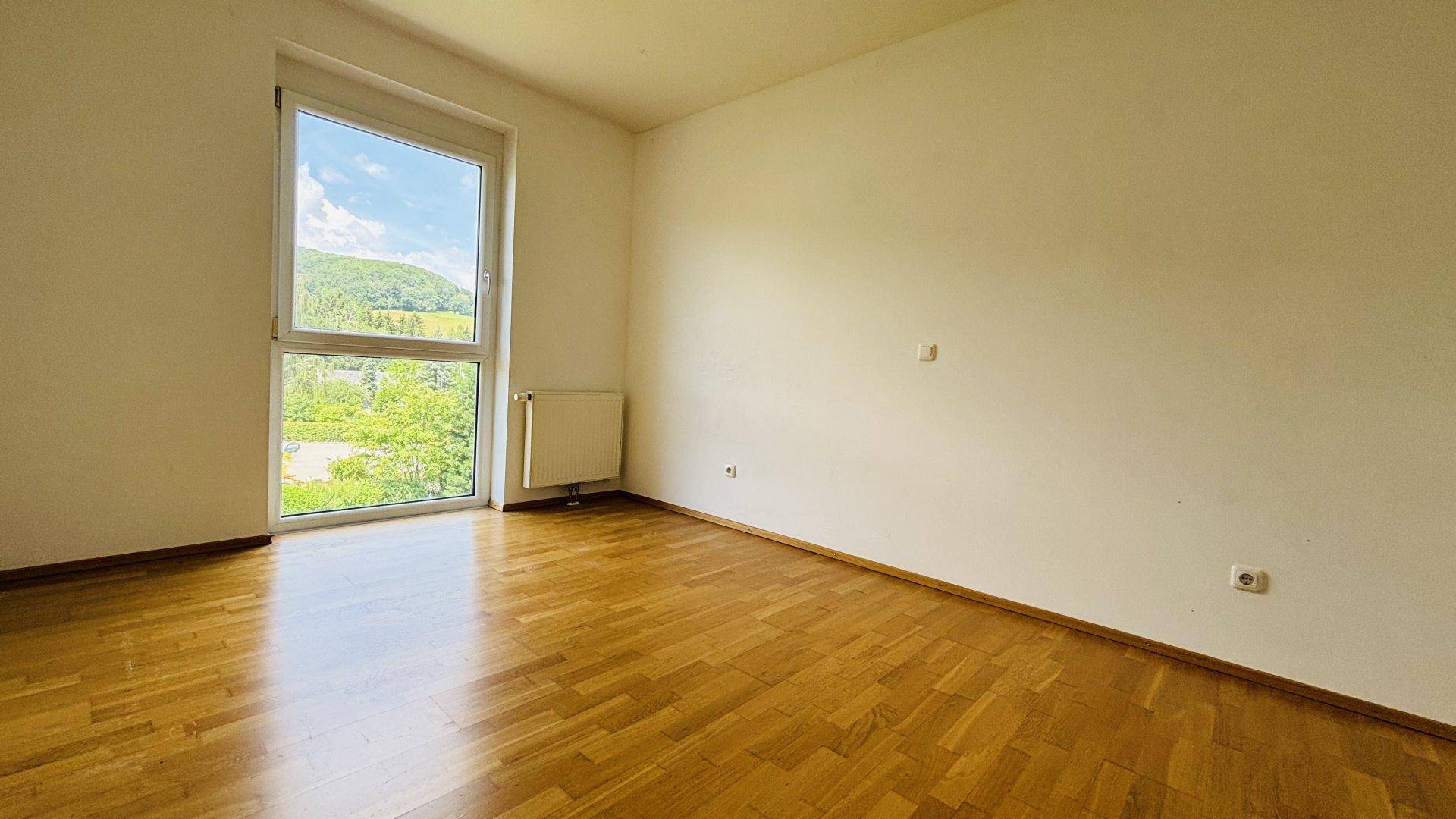 Geräumiges Schlafzimmer mit Holzboden und großem Fenster, das viel Tageslicht hereinlässt.