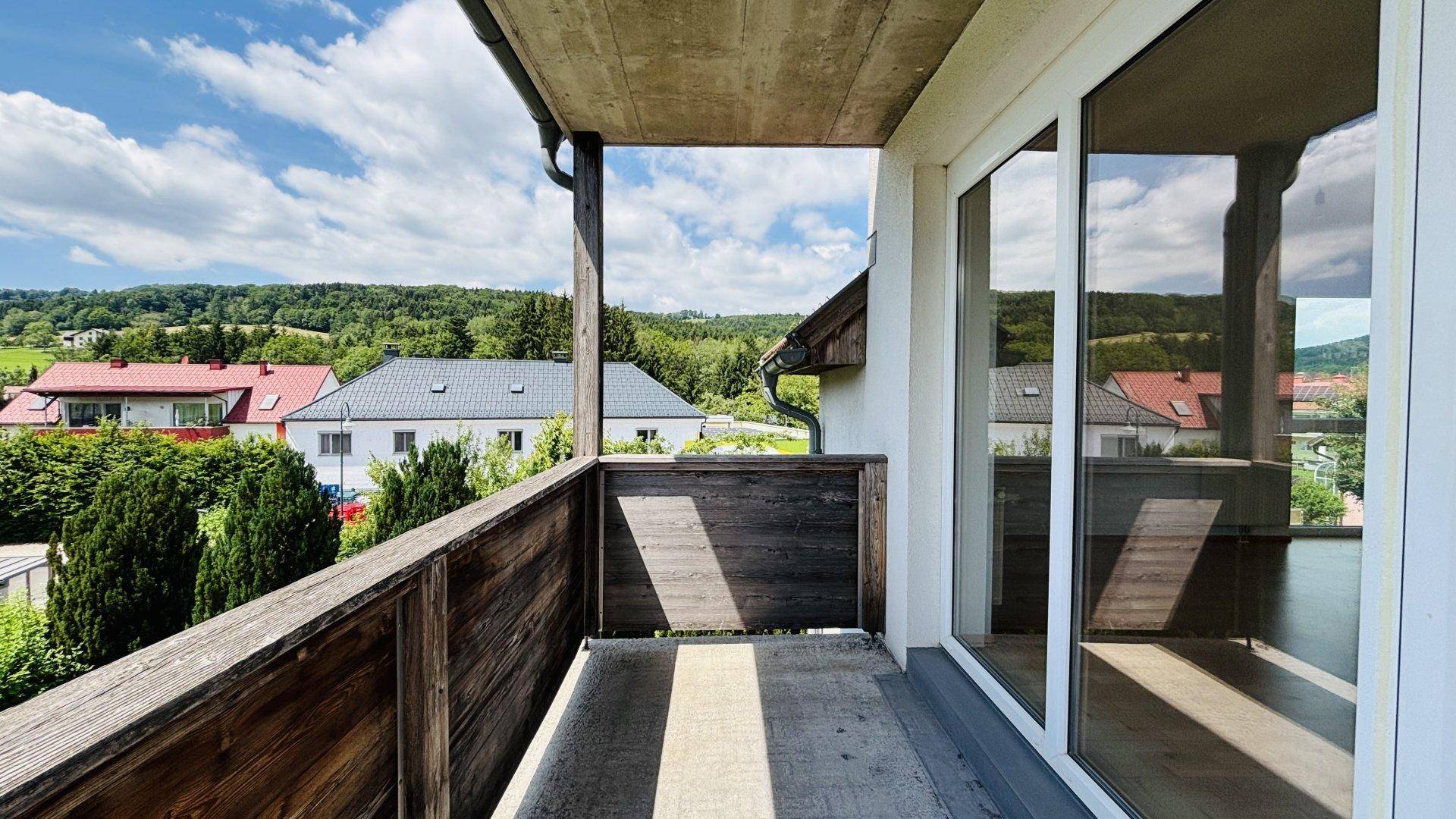 Balkon mit Holzboden und Glas-Schiebetüren, bietet einen schönen Ausblick auf die Umgebung.