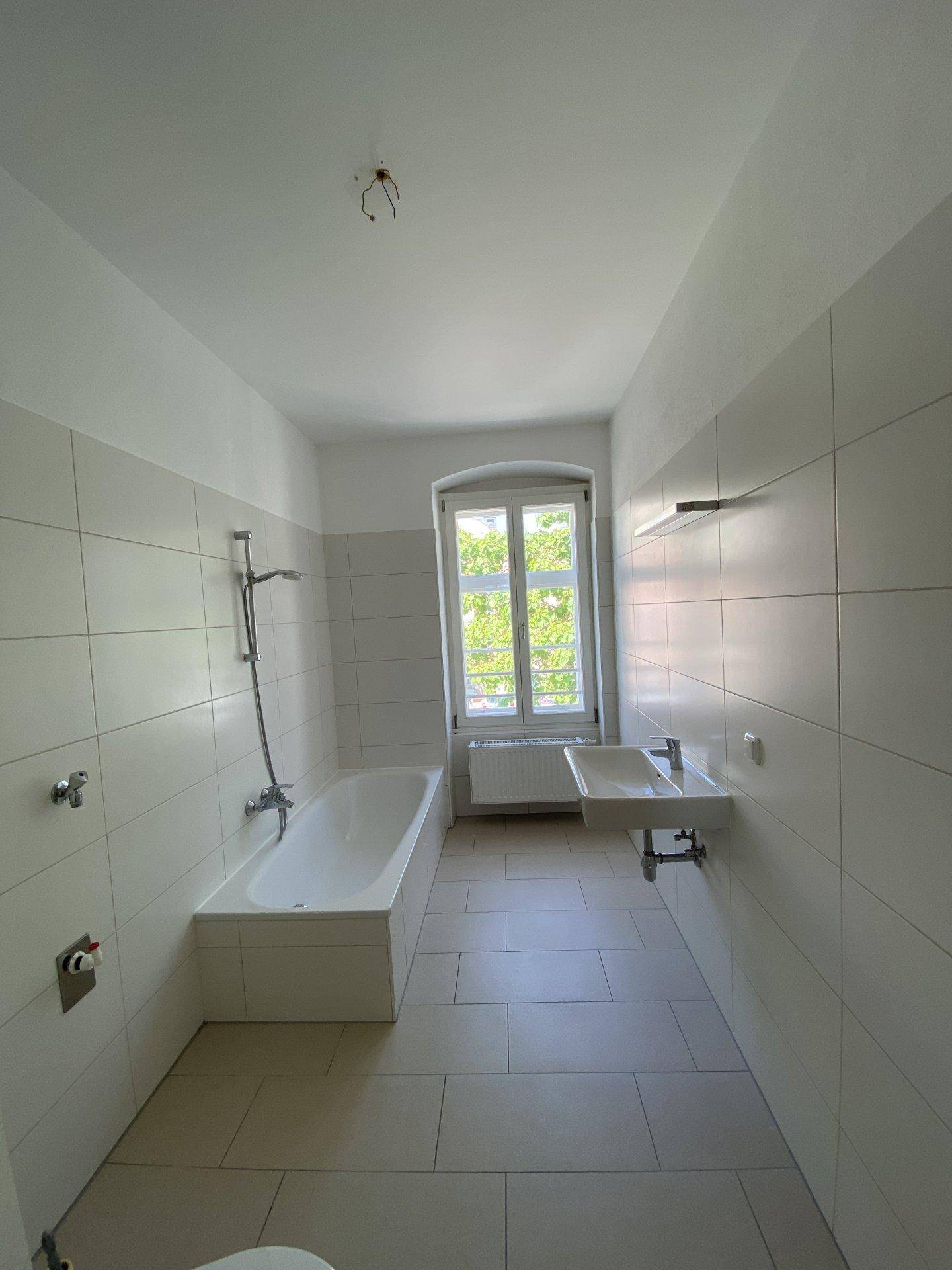 Helles Badezimmer mit Badewanne, Waschbecken, weißen Fliesen und Fenster.