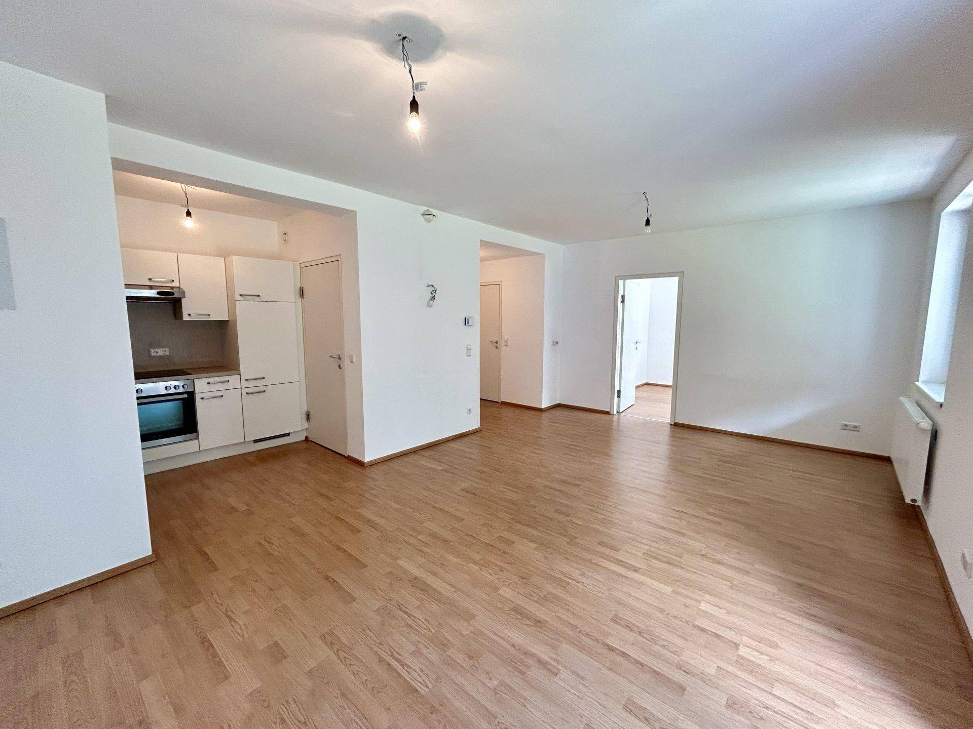 Heller Wohn-Essbereich mit Holzboden und integrierter Küchenzeile in weißem Design.