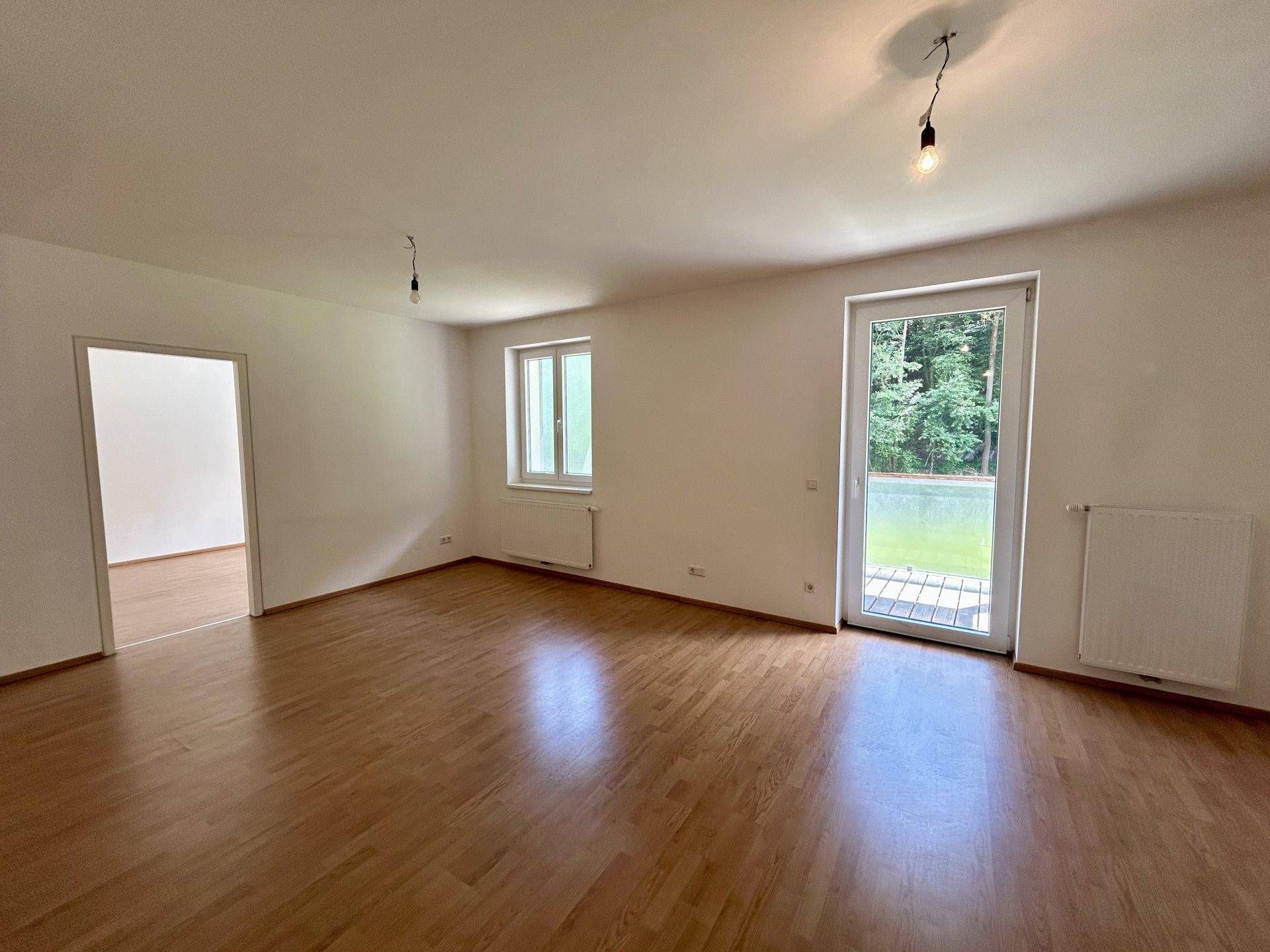 Geräumiges Wohnzimmer mit Holzboden und Zugang zu einer Terrasse oder einem Gartenbereich.