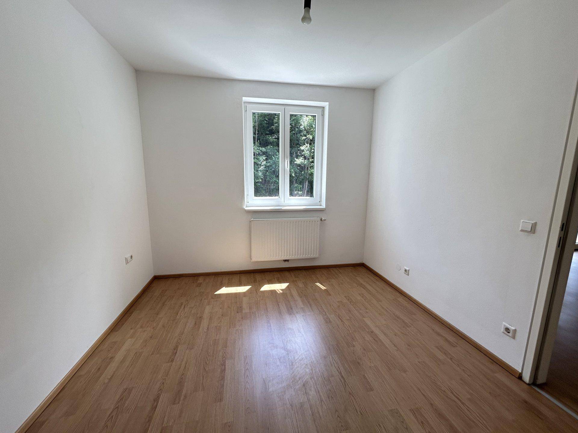 Helles Schlafzimmer mit Holzboden und Fenster mit Blick ins Grüne.