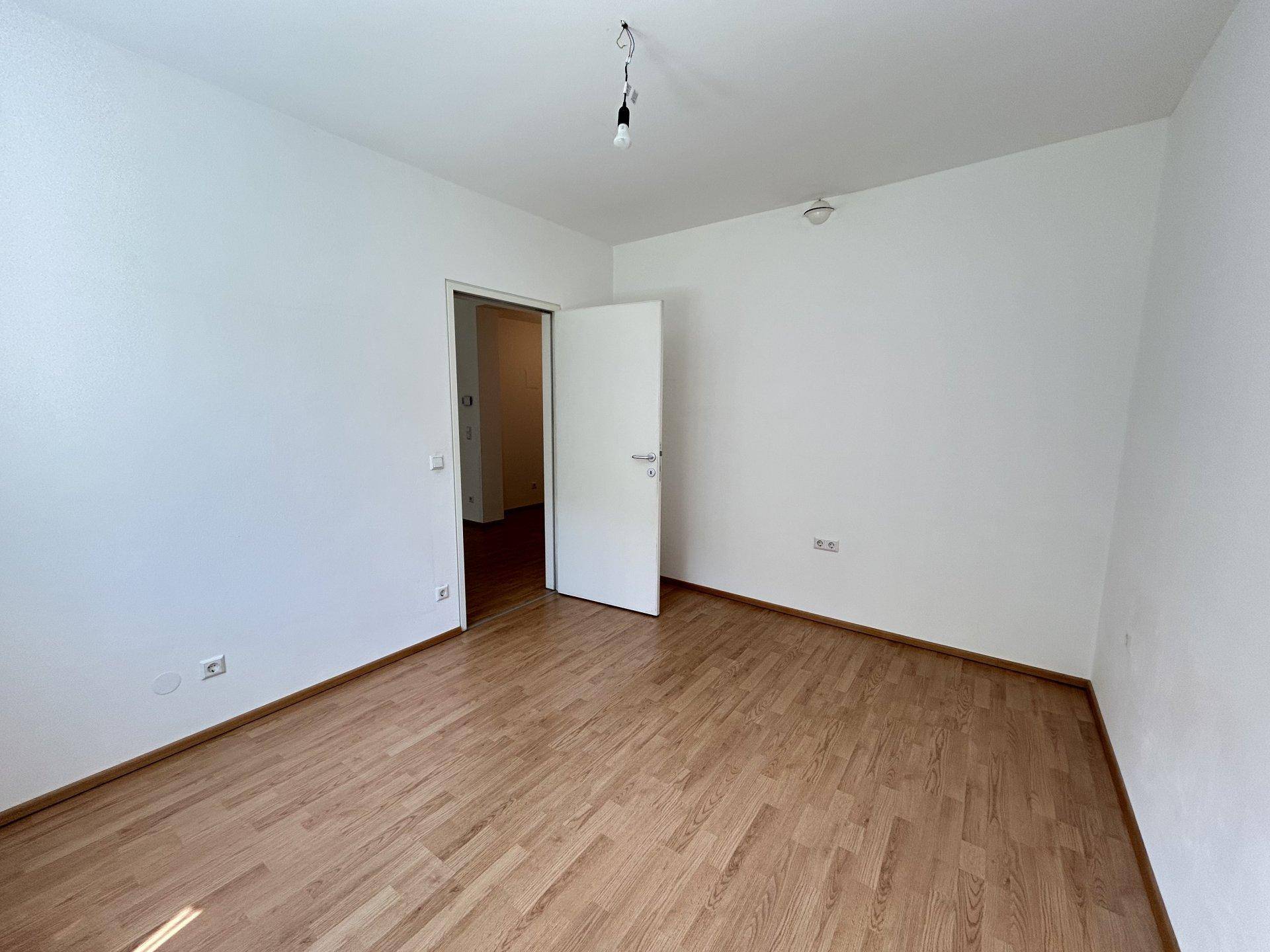 Leeres Schlafzimmer mit Holzboden und weiß gestrichenen Wänden, bereit zur Einrichtung.