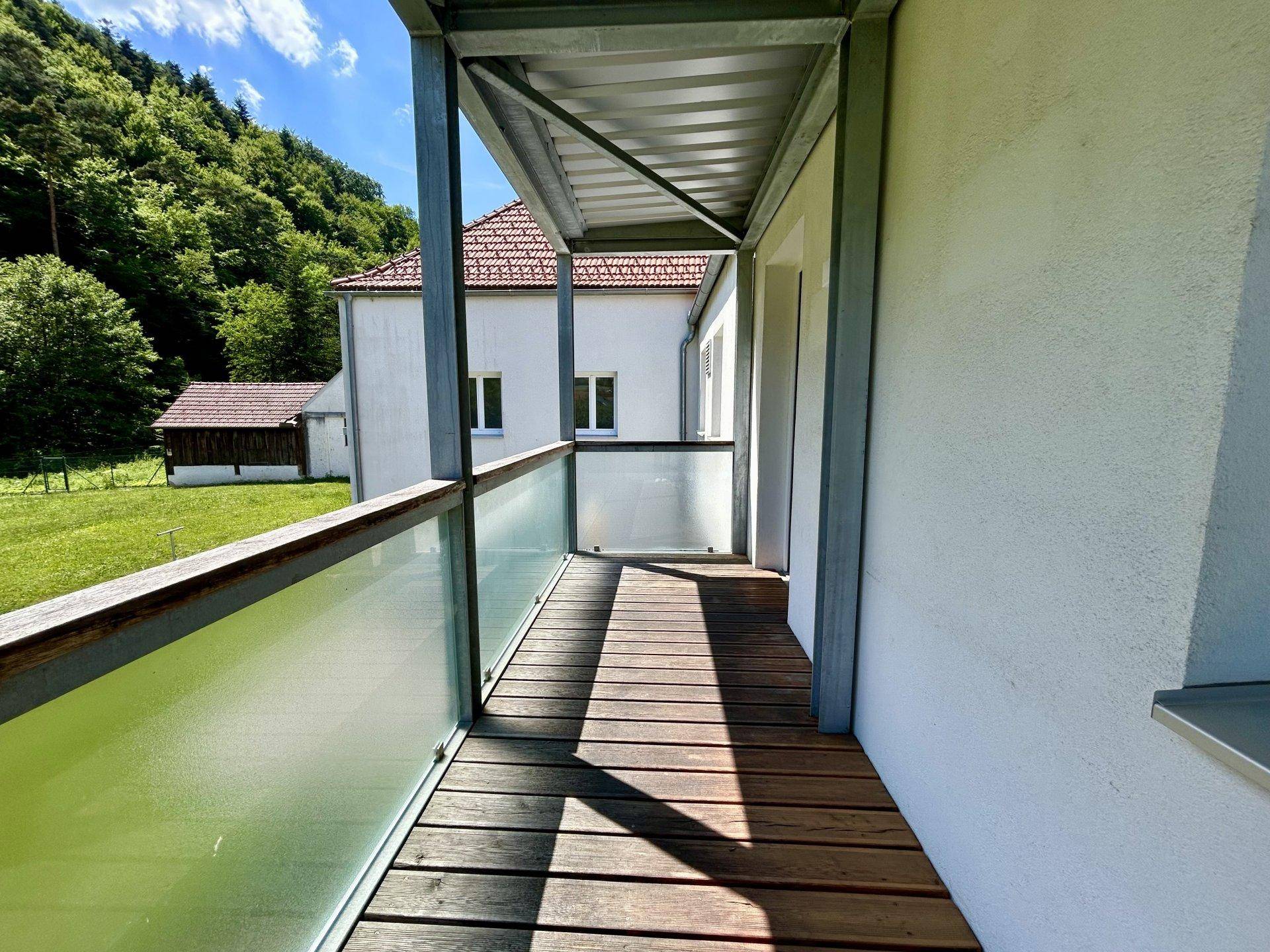 Überdachter Balkon mit Holzboden und Glasgeländer, bietet Blick auf die Umgebung.