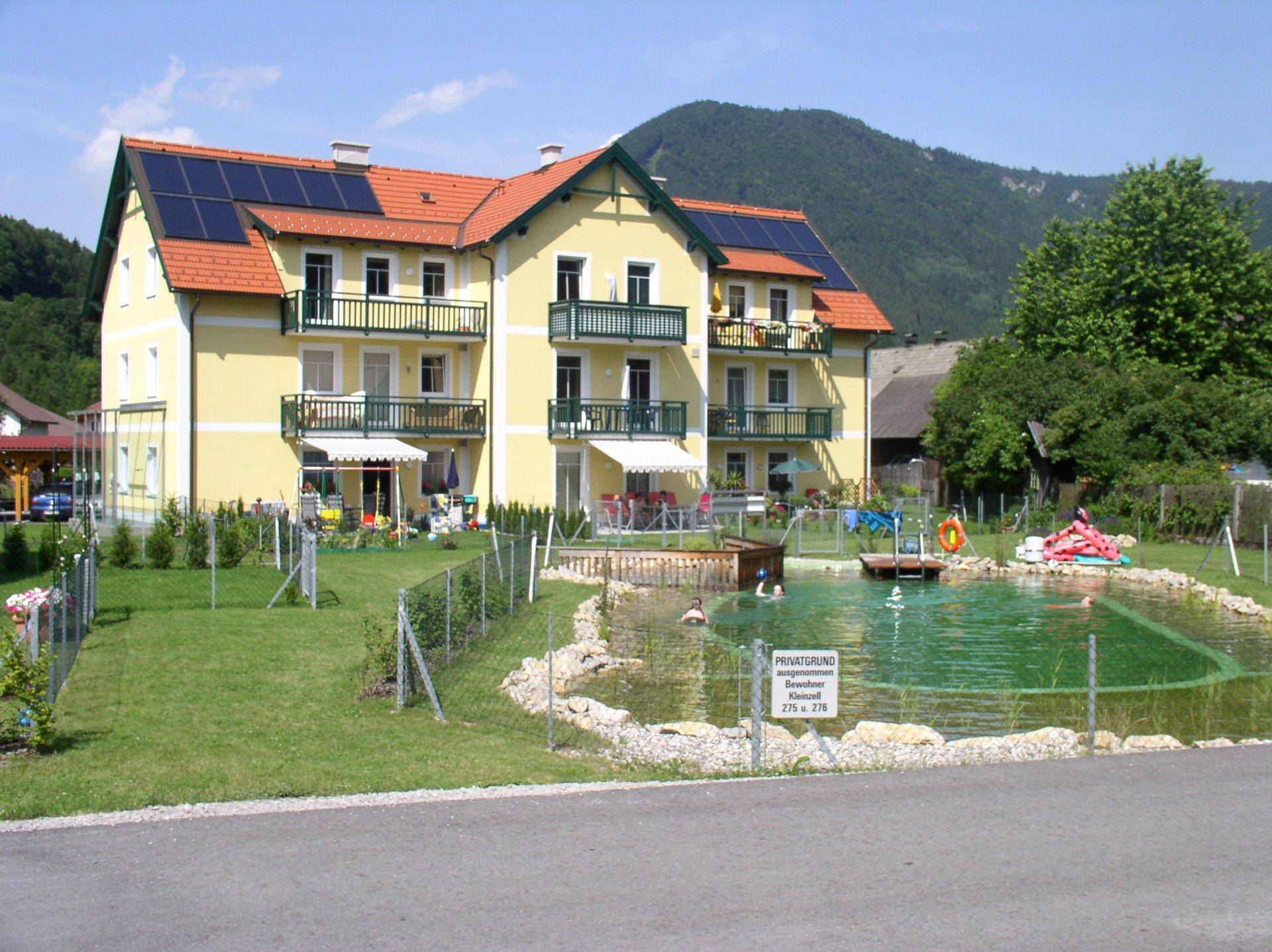 Mehrere gelbe Wohngebäude mit Balkonen, einem Naturschwimmteich und einem Spielplatz.