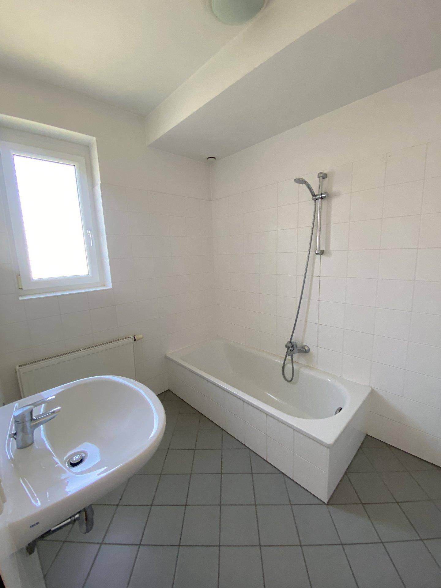 Helles Badezimmer mit weißen Wandfliesen, Badewanne und einem einzelnen Waschbecken.