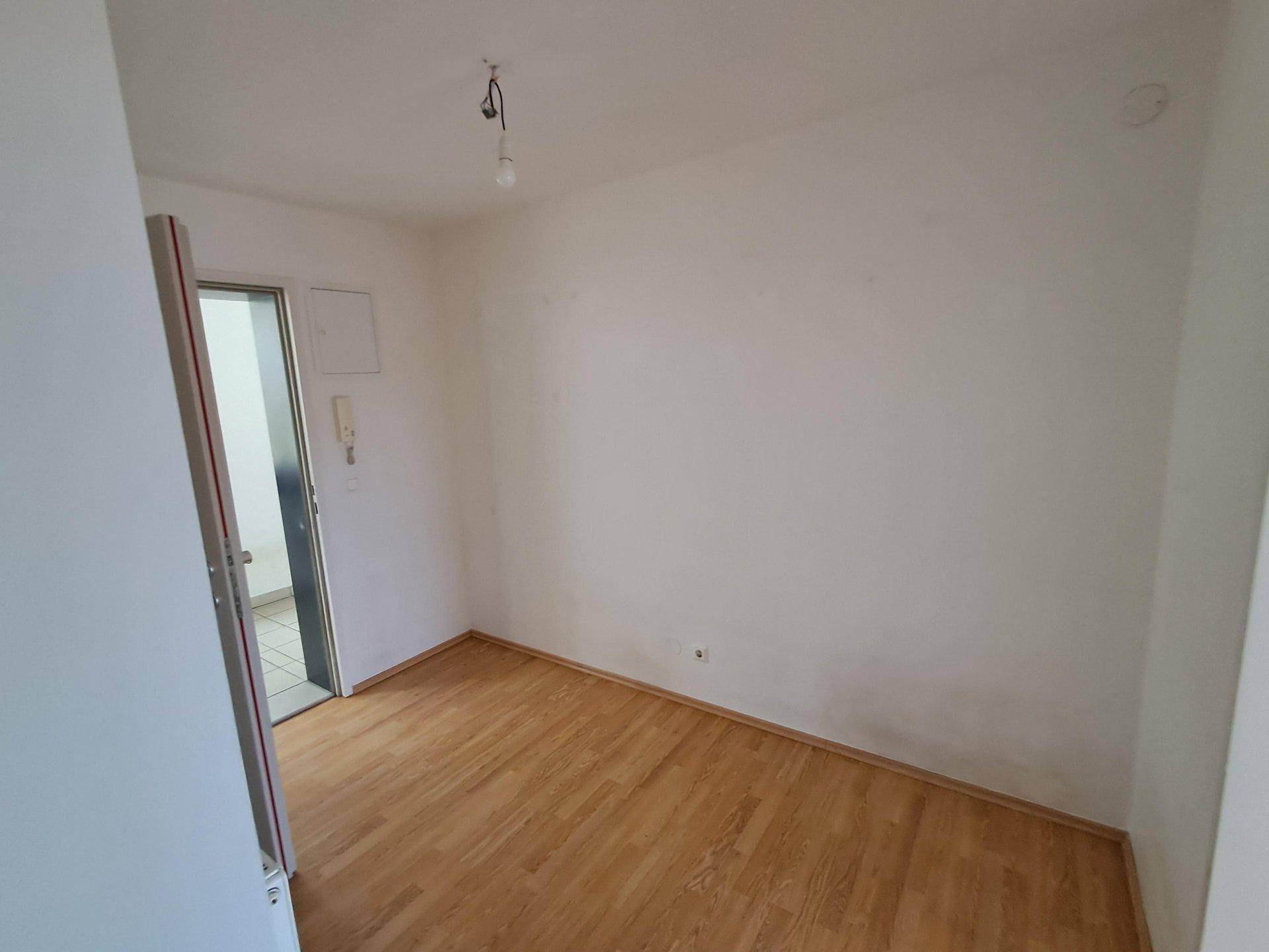 Leeres Zimmer mit hellem Laminatboden und Zugang zu einem Außenbereich.
