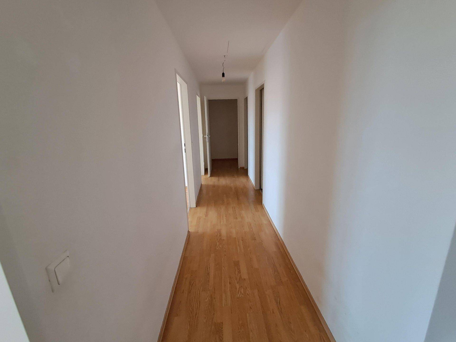 Langer, heller Flur mit Laminatboden und mehreren Türen zu angrenzenden Räumen.
