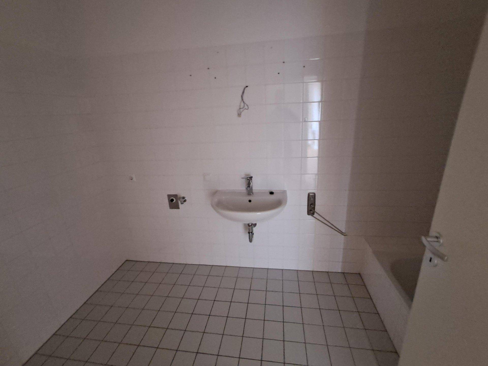 Helles Badezimmer mit weißen Fliesen, Waschbecken und Platz für eine Badewanne.