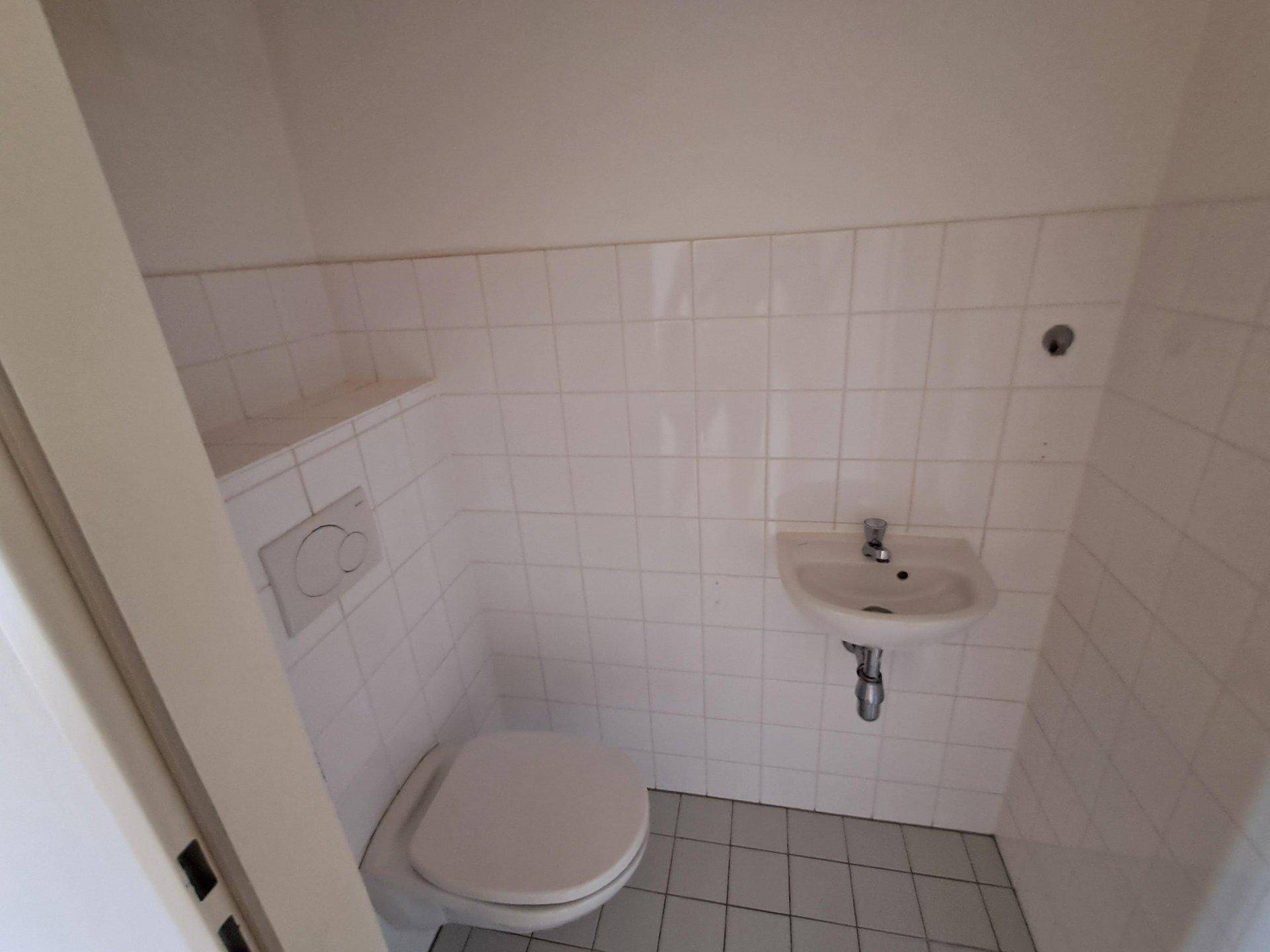 Kleines Gäste-WC mit weißen Fliesen, Toilette und Handwaschbecken.