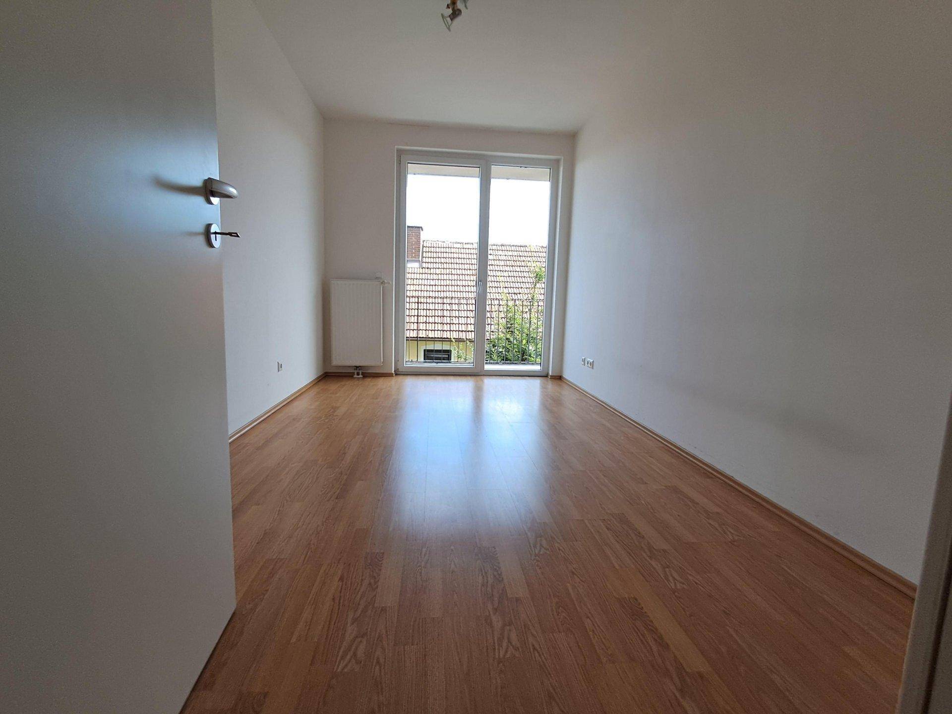 Geräumiges Schlafzimmer mit Laminatboden und viel Tageslicht durch die Balkontür.