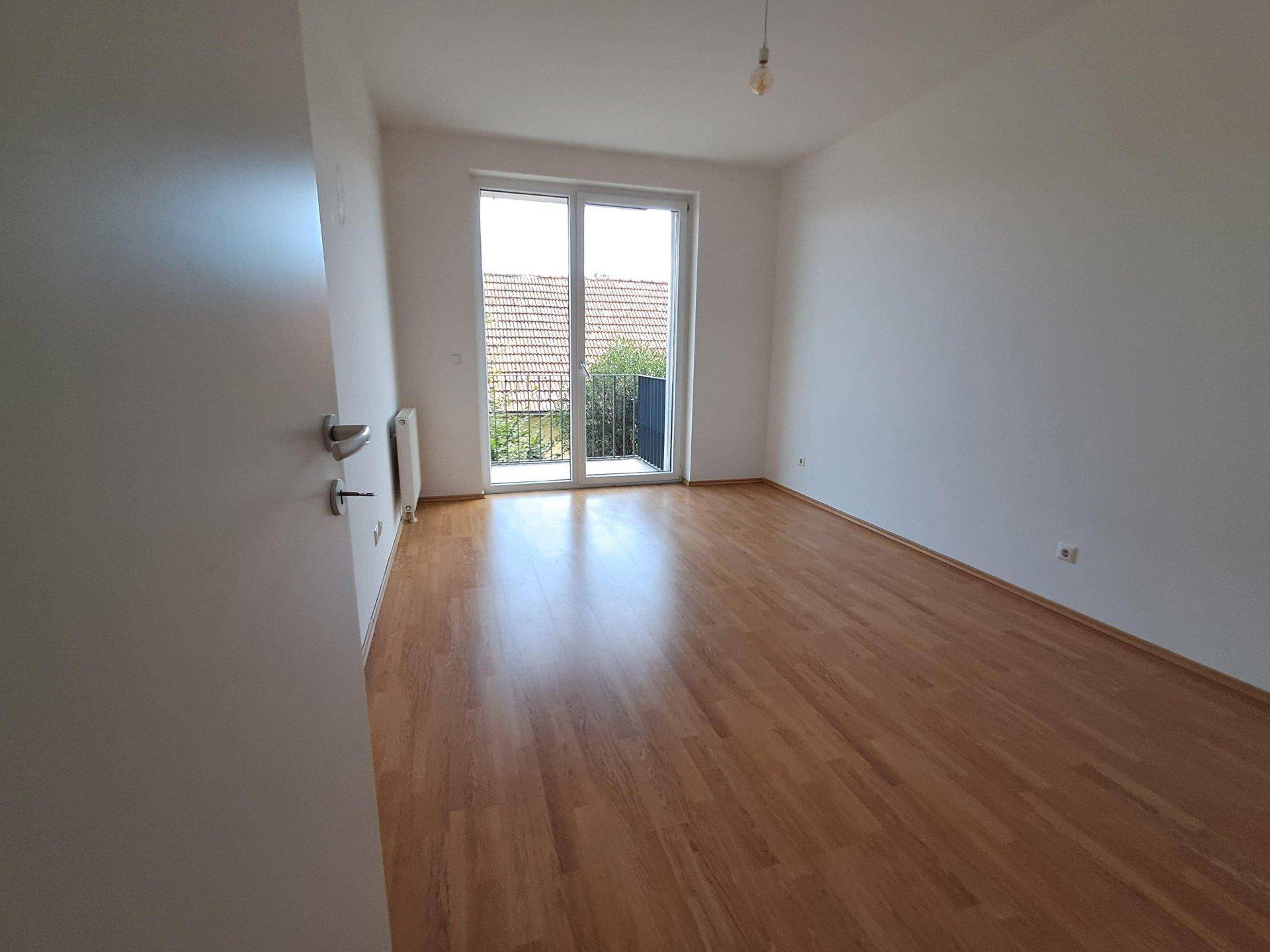 Helles Schlafzimmer mit Laminatboden und großem Fenster mit Zugang zum Balkon.