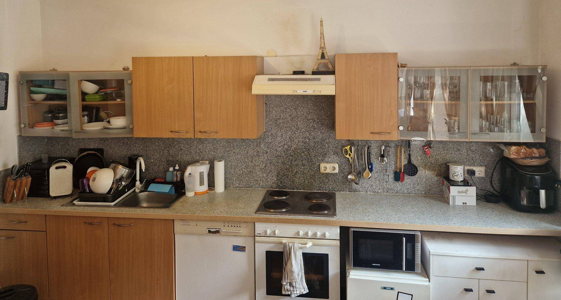 Funktionale Küche mit hellen Holzschränken, grauer Arbeitsplatte und integrierten Geräten.