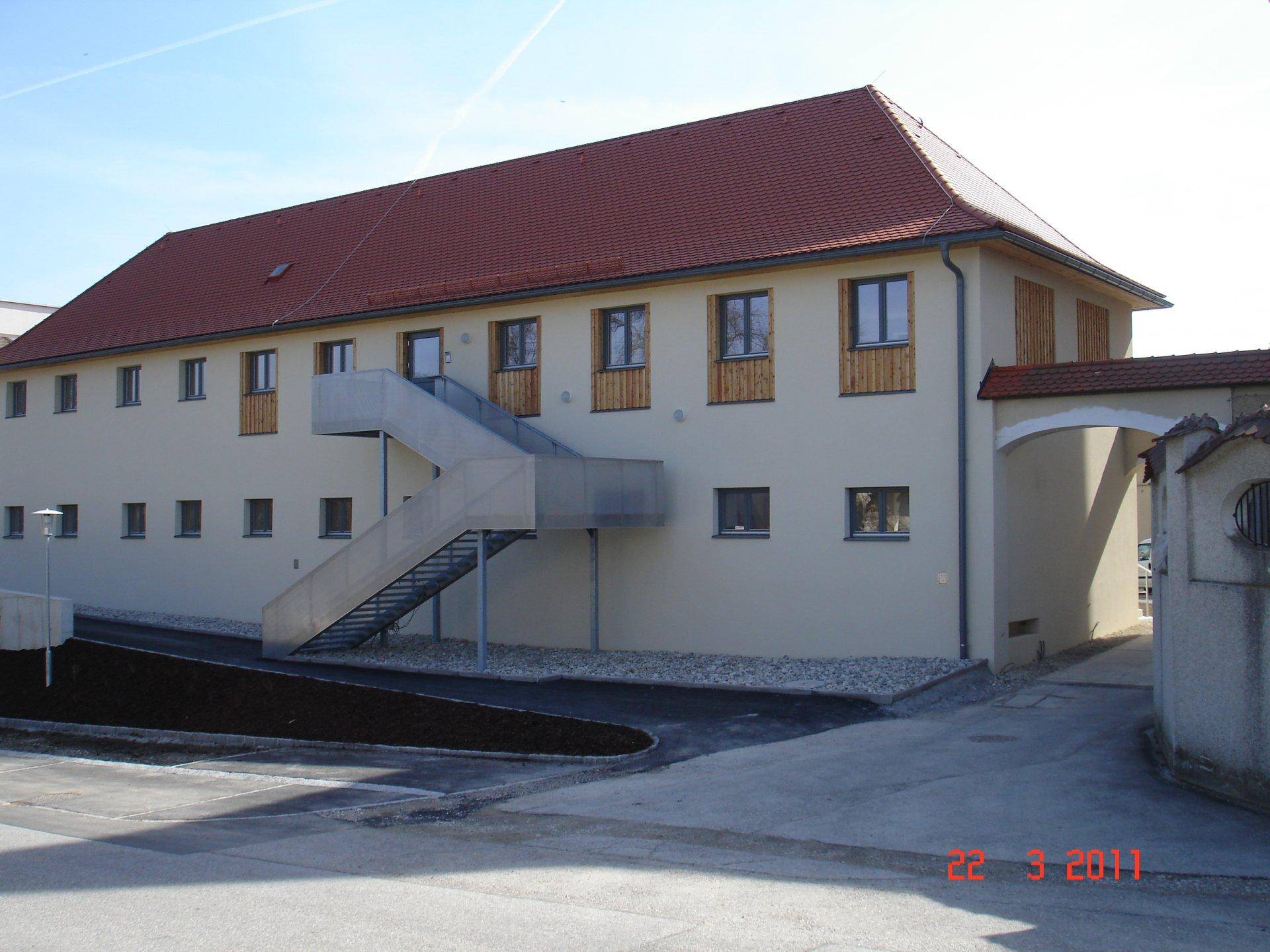 Beigefarbenes Gebäude mit rotem Ziegeldach und externer Metalltreppe für den Zugang.