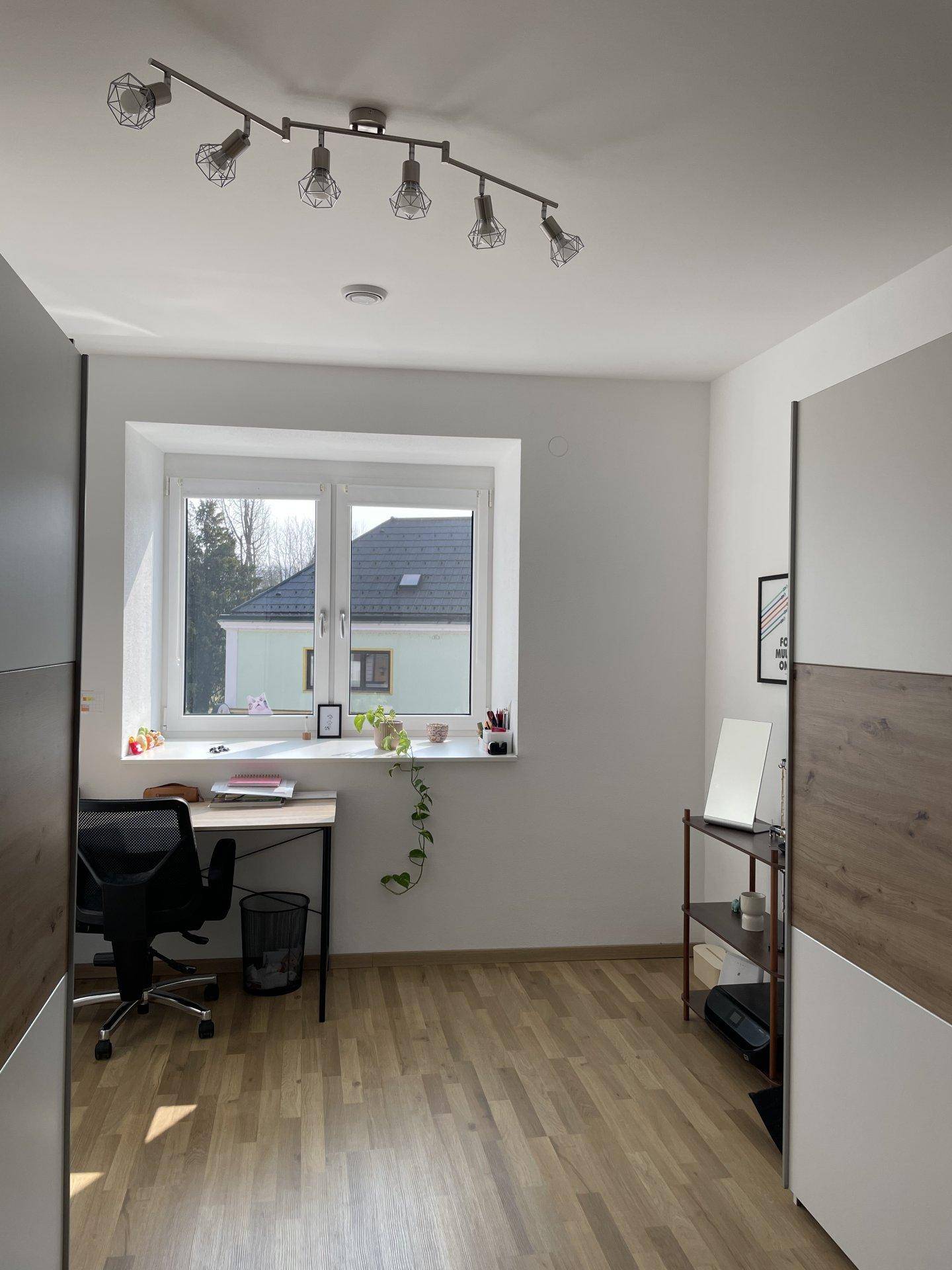 Helles Arbeitszimmer mit Schreibtisch, Stuhl und Fenster, das viel Tageslicht hereinlässt.