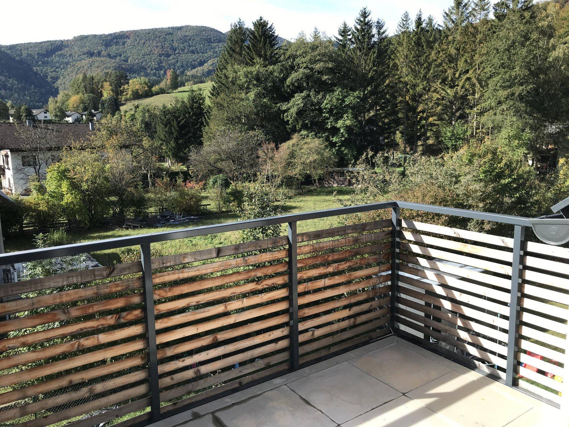 Sonniger Balkon mit Fliesenboden und Holzzaun, der eine malerische Aussicht auf die grüne Landschaft bietet.