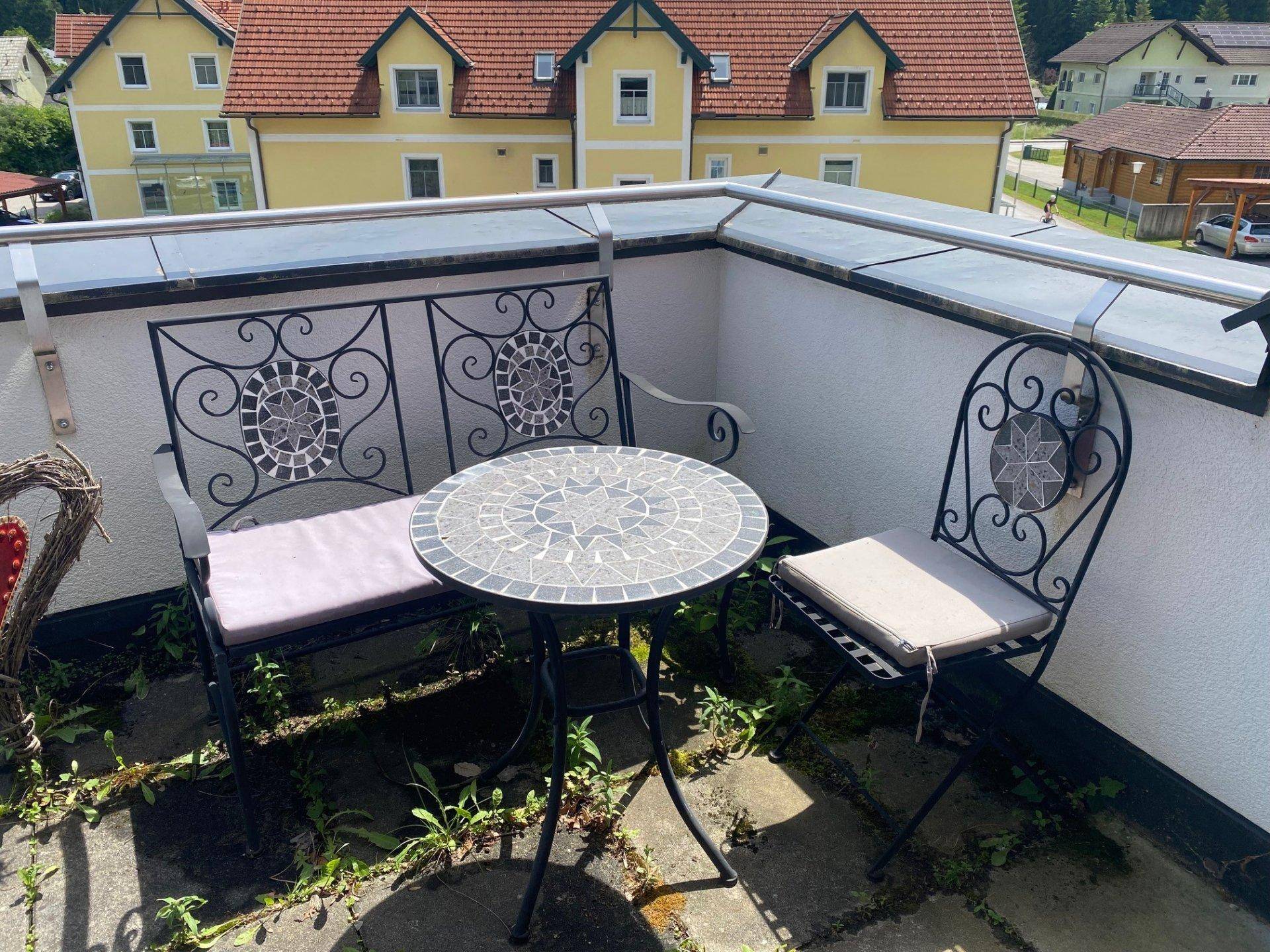 Kleiner Sitzbereich mit Mosaiktisch und Stühlen auf einem Balkon mit Blick auf die Nachbarschaft.