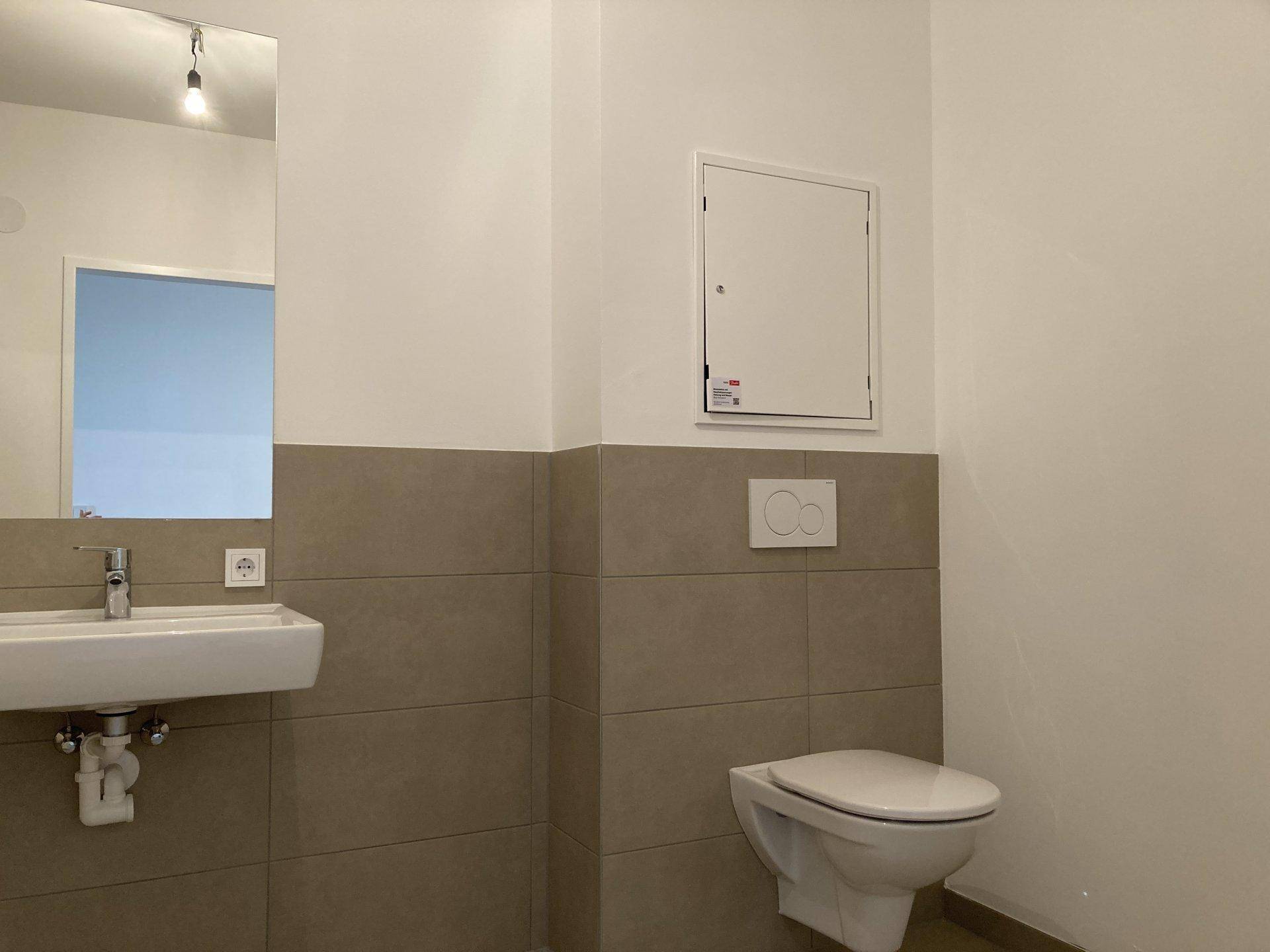 Modernes Gäste-WC mit Wand-WC, Waschbecken und beigefarbenen Fliesen an der Wand, in neuwertigem Zustand.