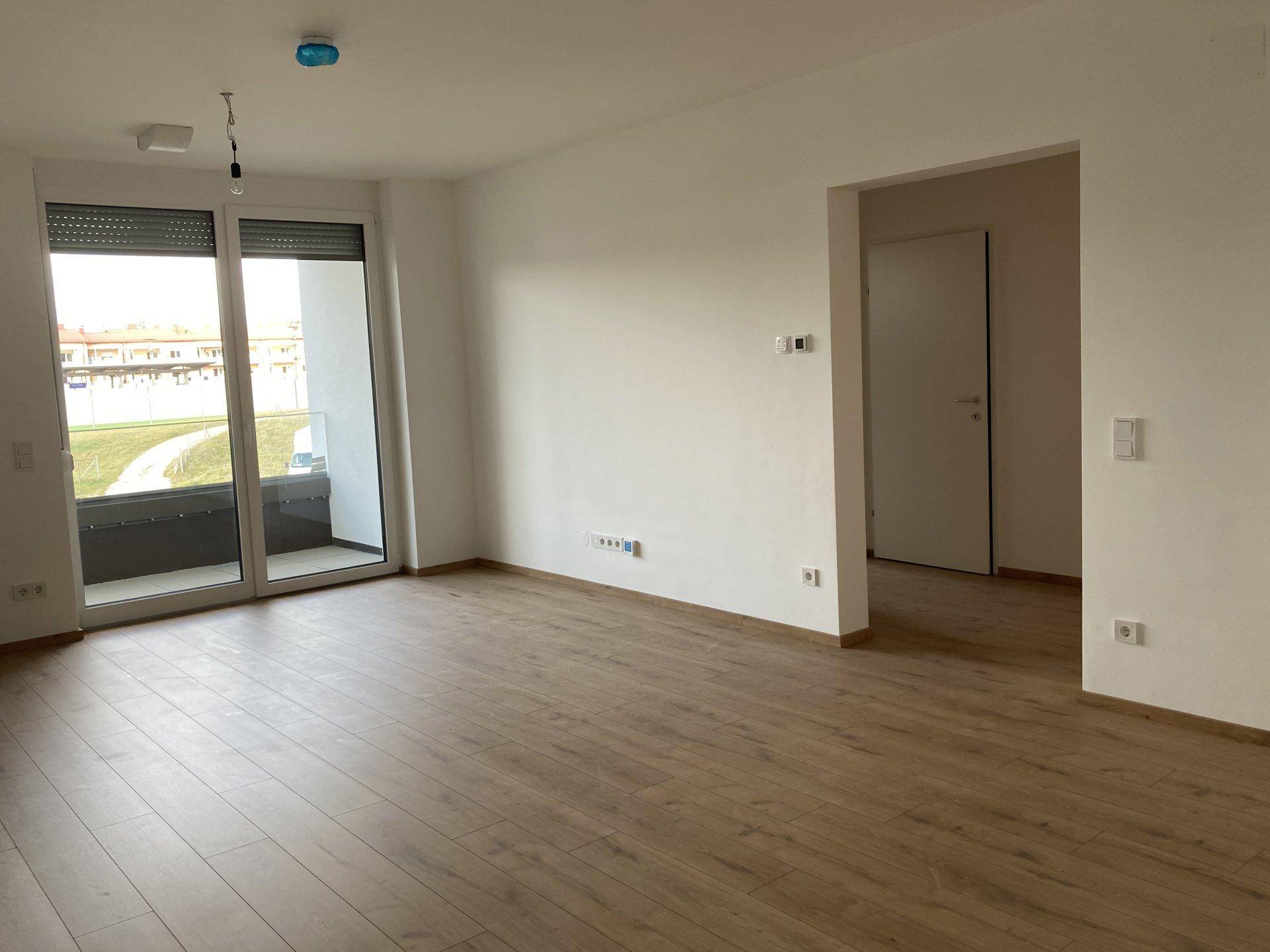 Helles Wohnzimmer mit Laminatboden und Zugang zu einem Balkon durch große Schiebetüren mit Rollläden.