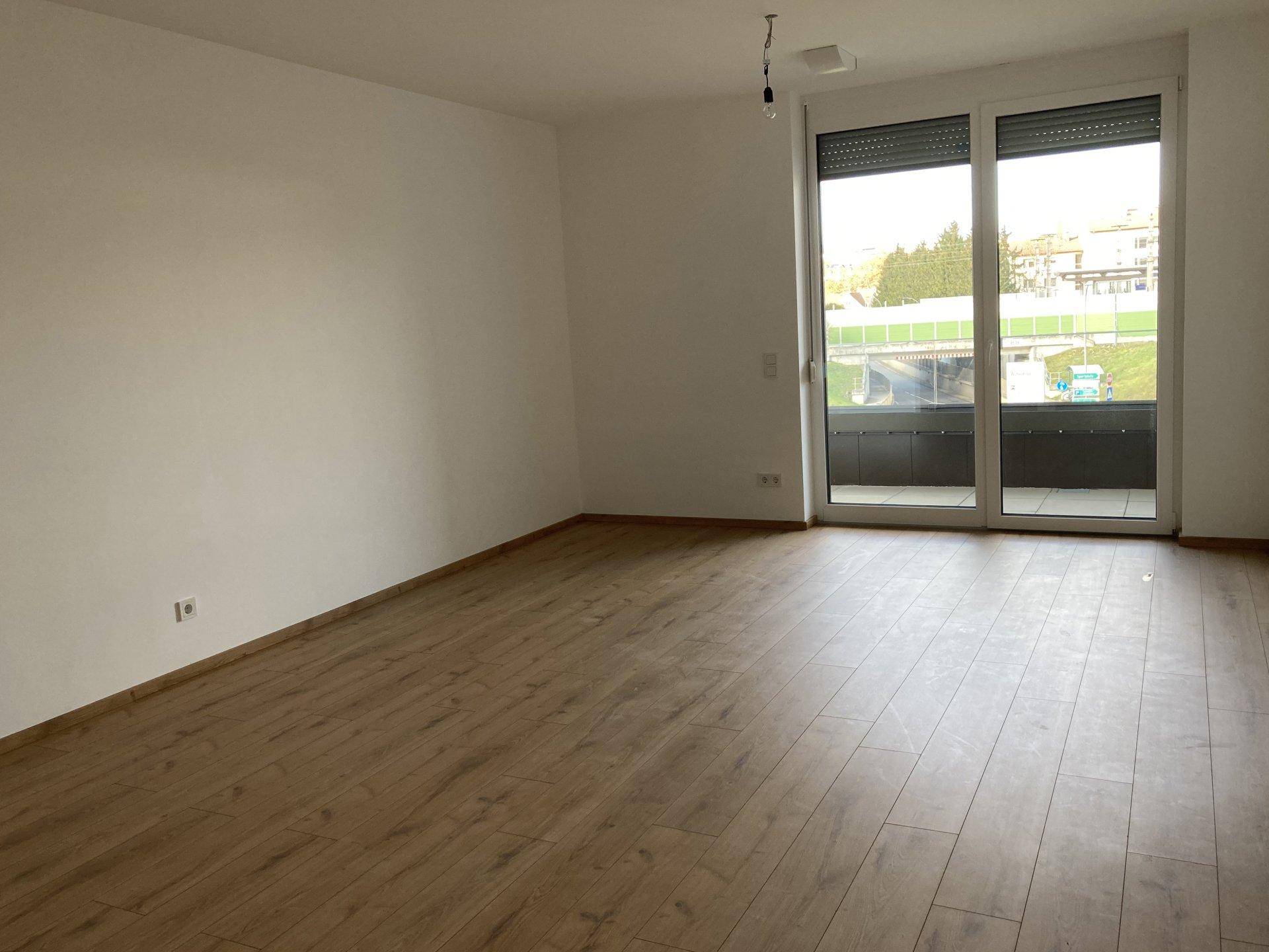 Helles Zimmer mit Laminatboden und großem Fenster mit Zugang zu einem Balkon, in neuwertigem Zustand.