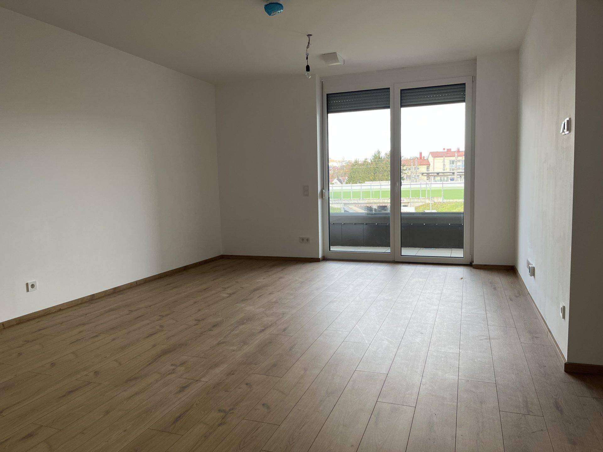 Geräumiges Wohnzimmer mit hellem Laminatboden und großen Fenstern zum Balkon, bereit zum Einzug.