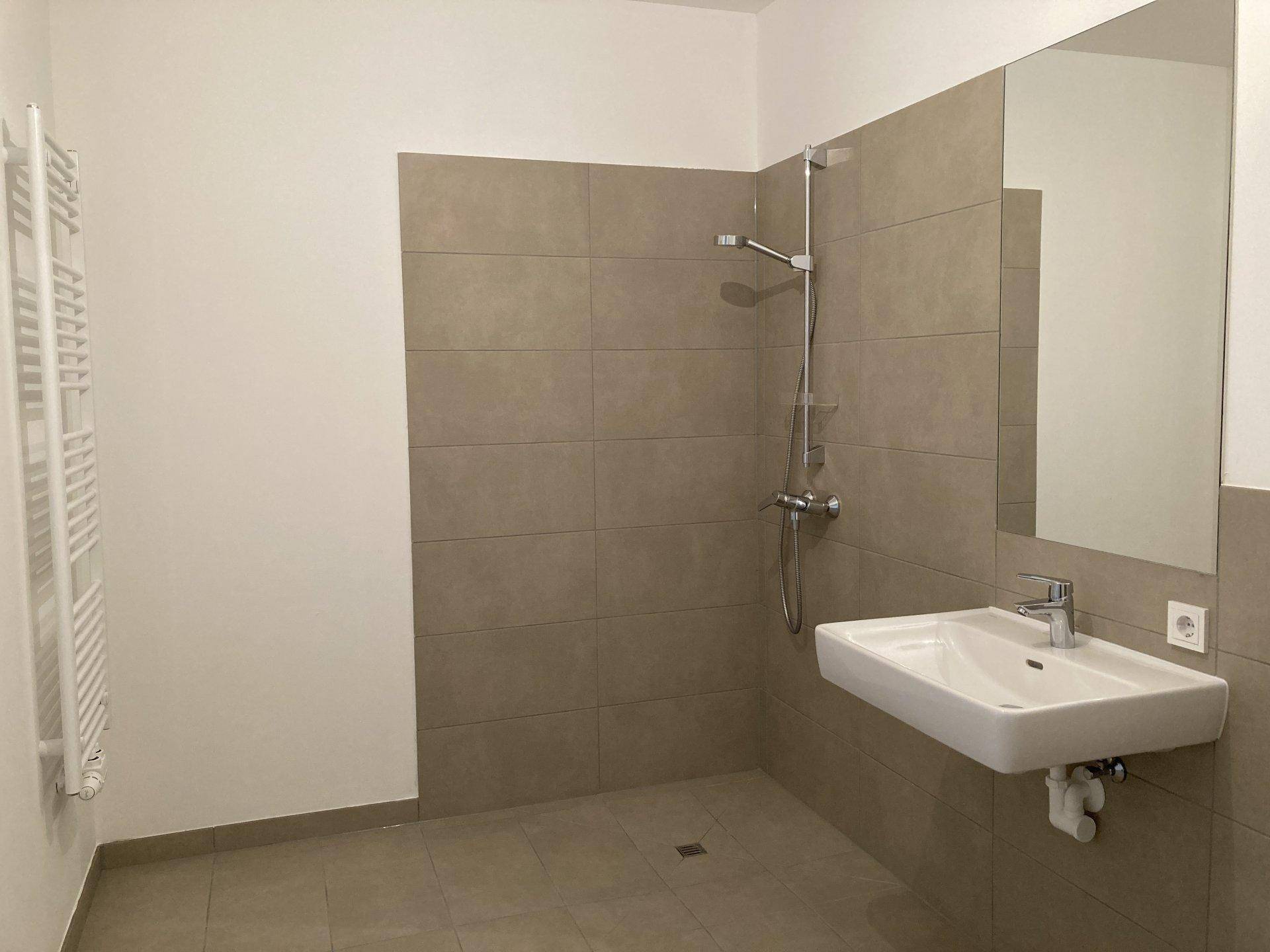 Modernes Badezimmer mit ebenerdiger Dusche, Waschbecken und beheiztem Handtuchhalter, in neuwertigem Zustand.