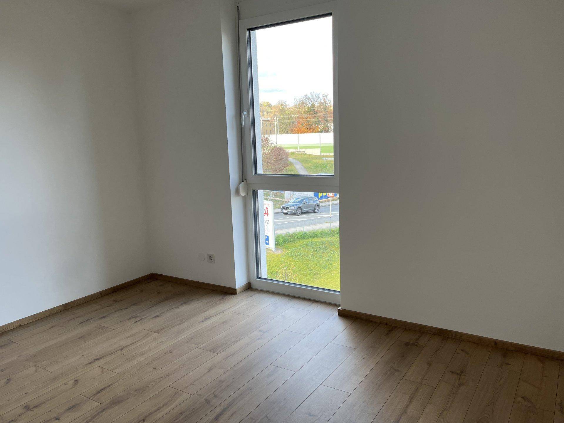 Helles Zimmer mit Laminatboden und großem Fenster, das viel Tageslicht hereinlässt, ideal als Schlafzimmer.