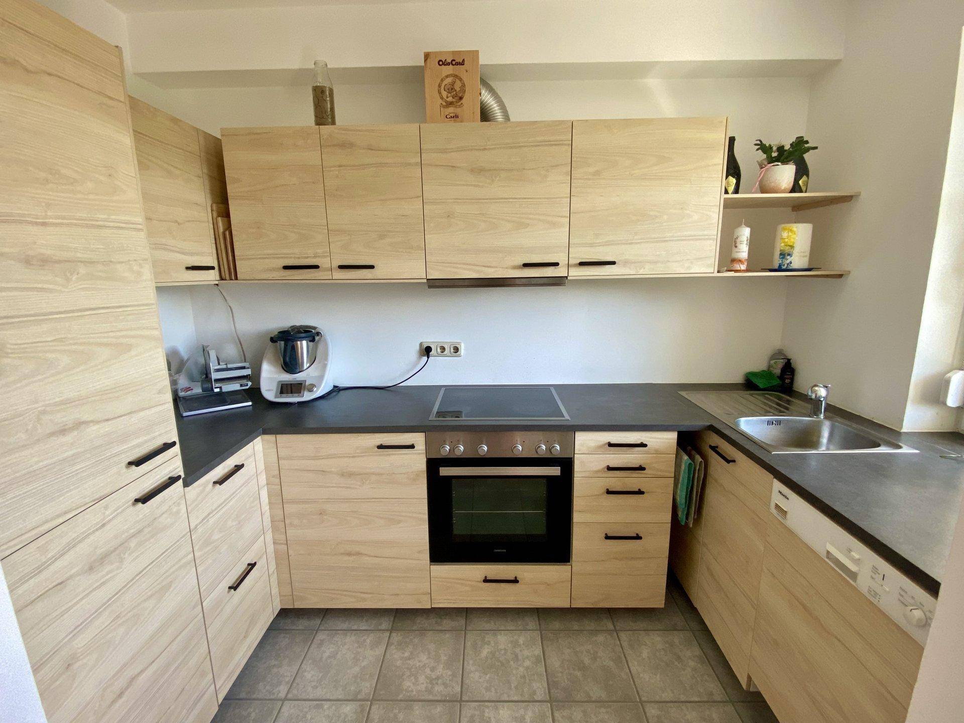 Moderne Einbauküche mit hellen Holzfronten, dunkler Arbeitsplatte und Fliesenboden.
