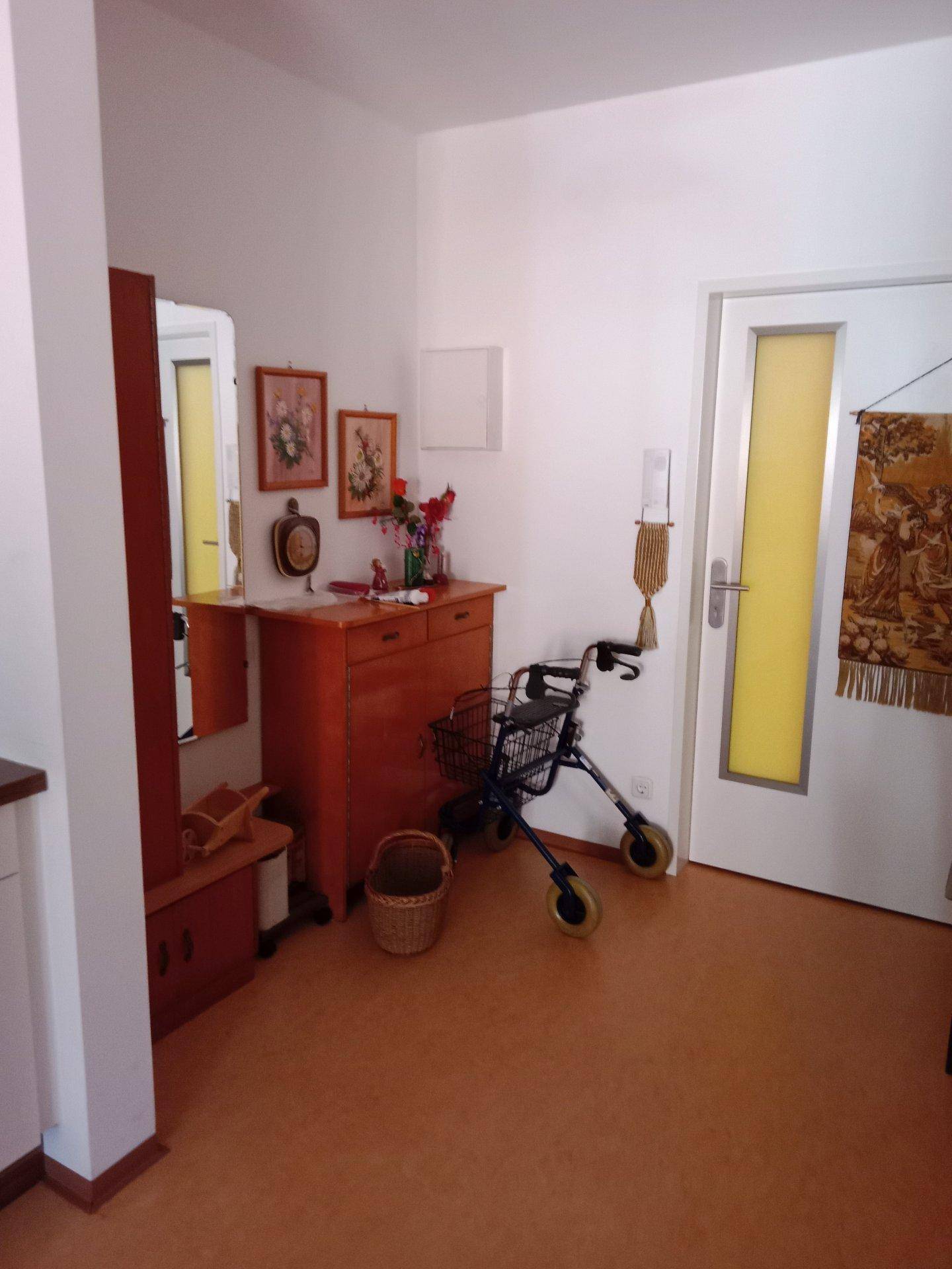 Heller Flur mit Garderobe, Spiegel und einem Rollator, der auf Barrierefreiheit hindeutet.