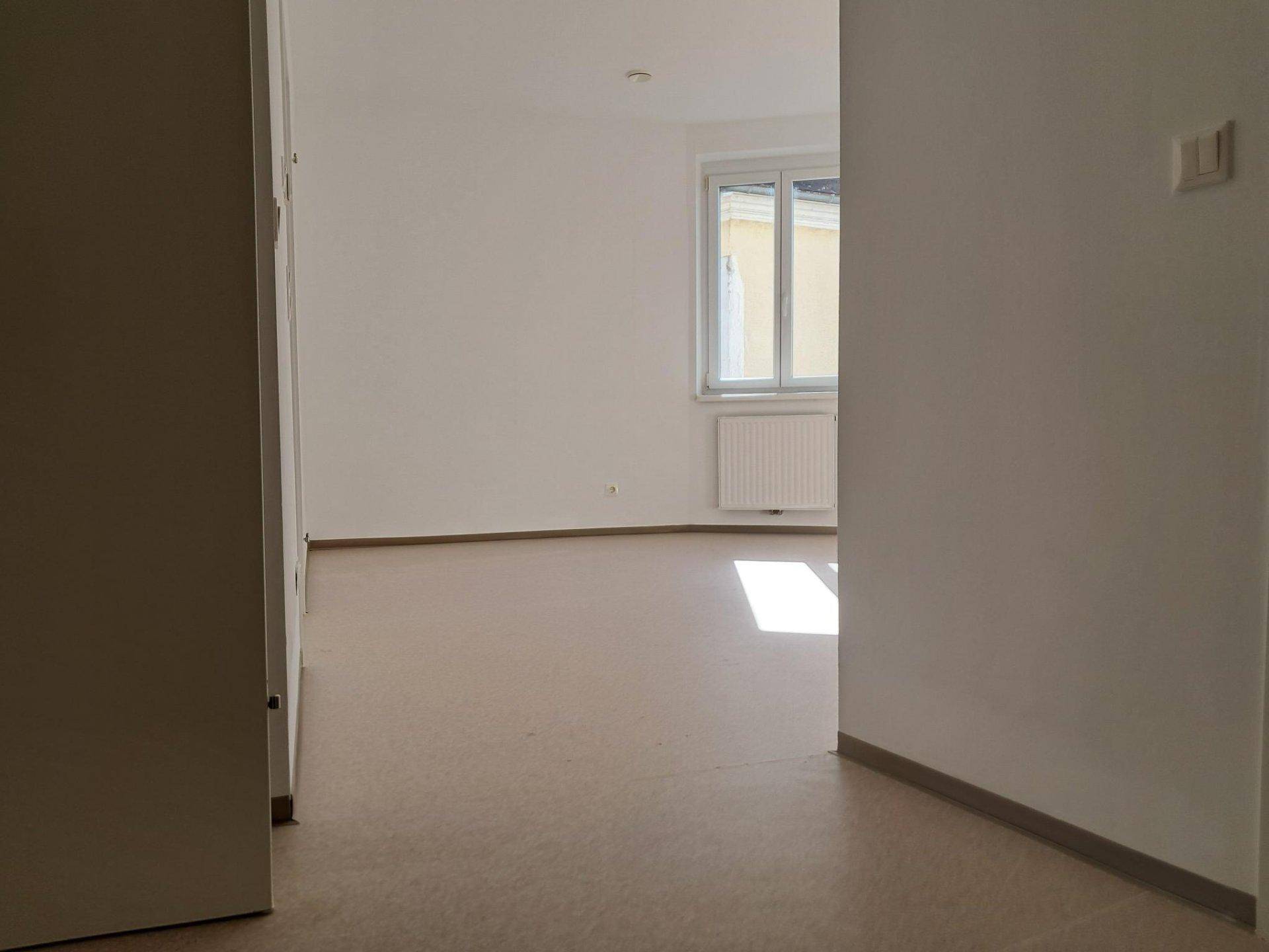 Heller, leerer Raum mit neutralen Wänden und einem Fenster, das Tageslicht hereinlässt.
