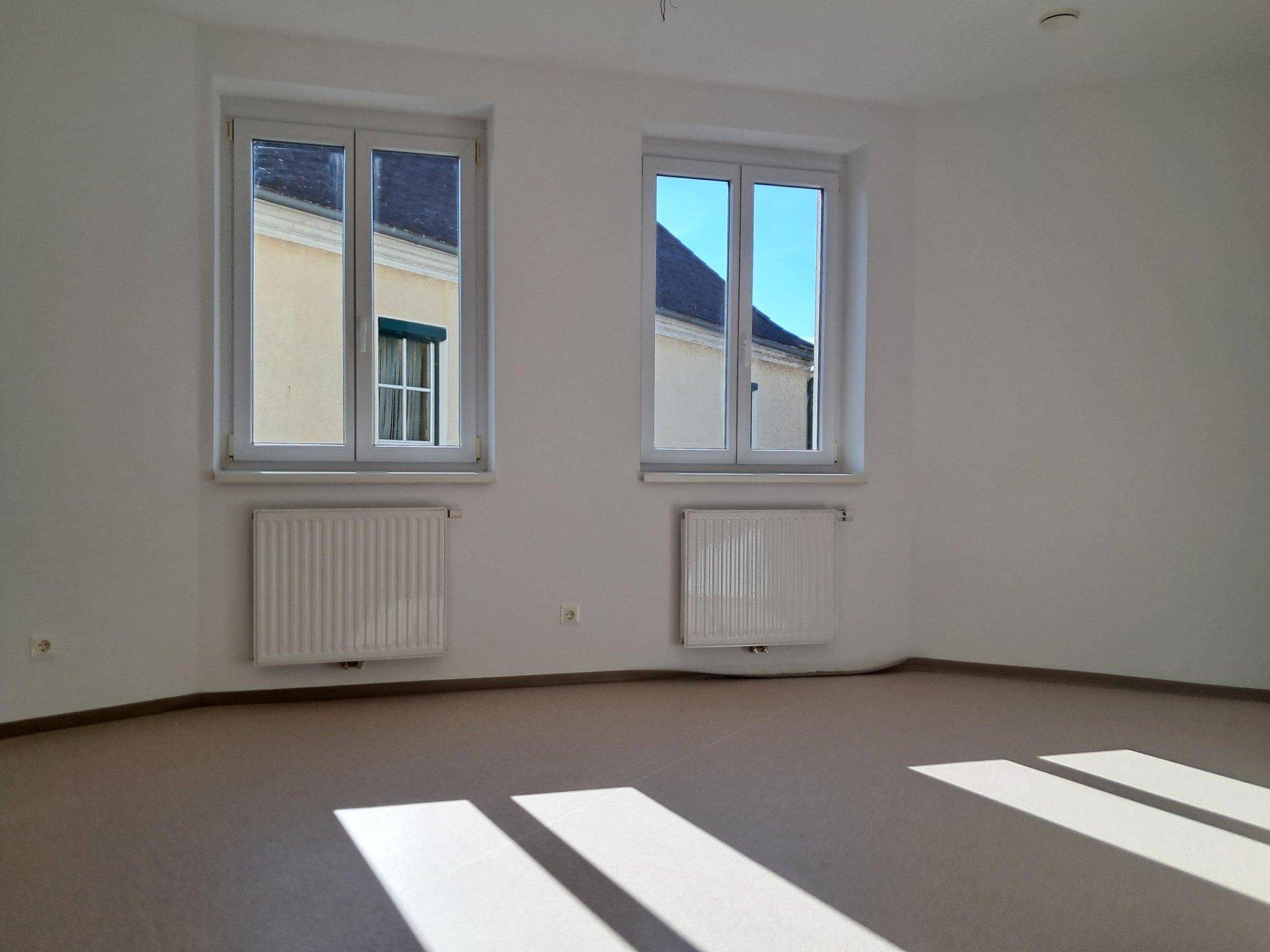Geräumiger, heller Wohnraum mit zwei großen Fenstern und viel natürlichem Lichteinfall.
